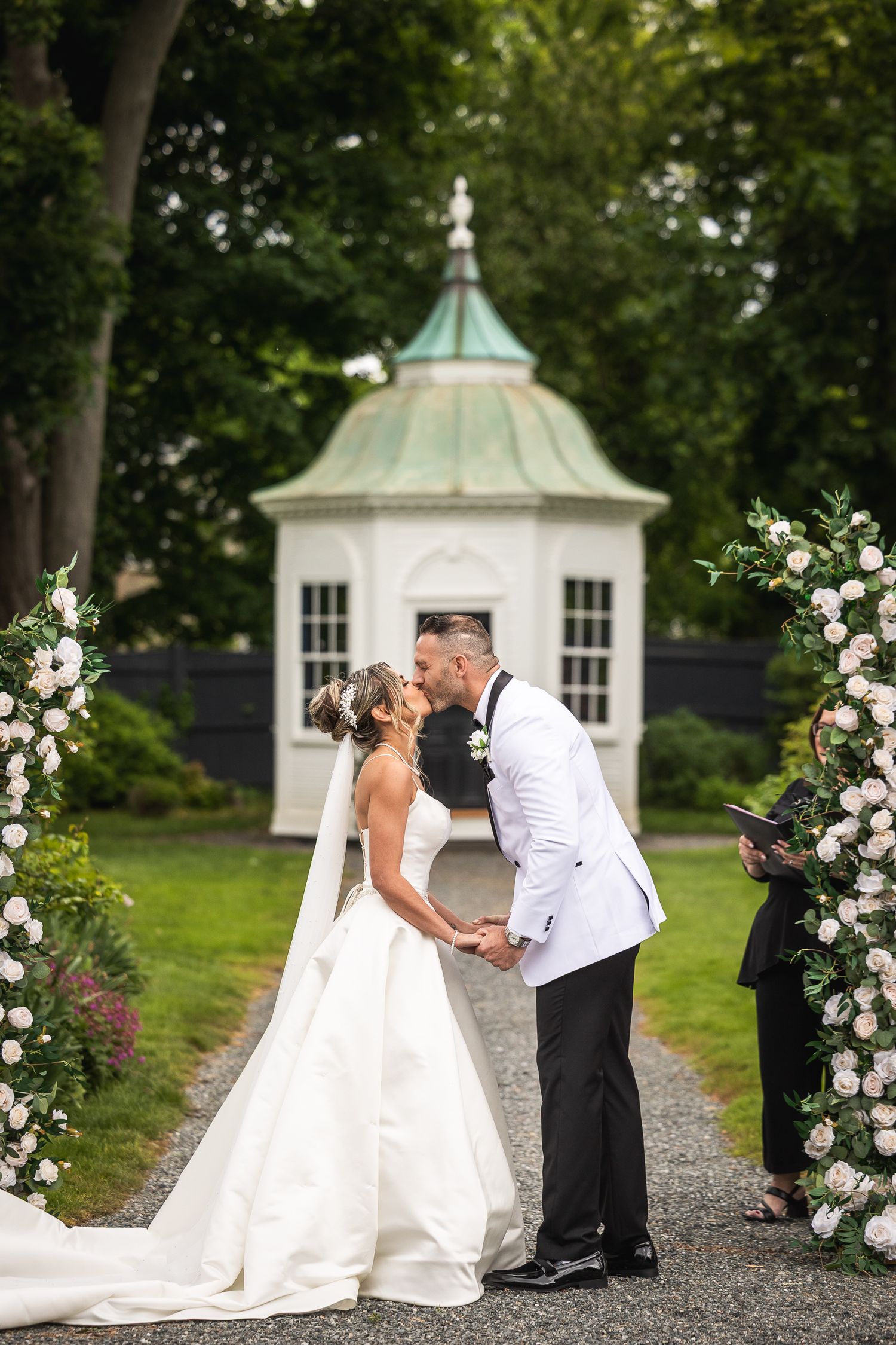Wedding couple shares intimate moments along garden path with gazebo in background.