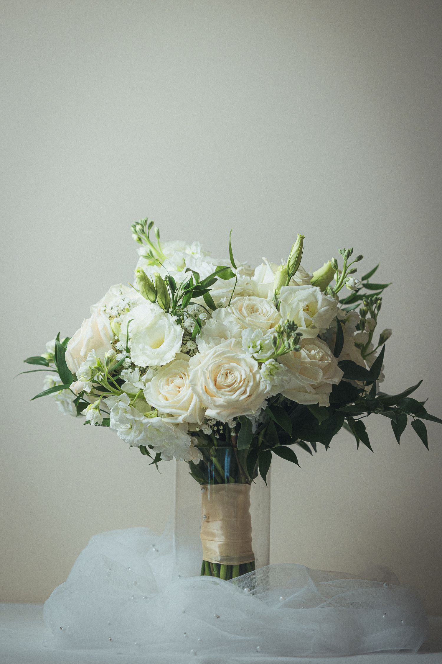Classic white rose wedding bouquet with greenery and delicate tulle wrapping.