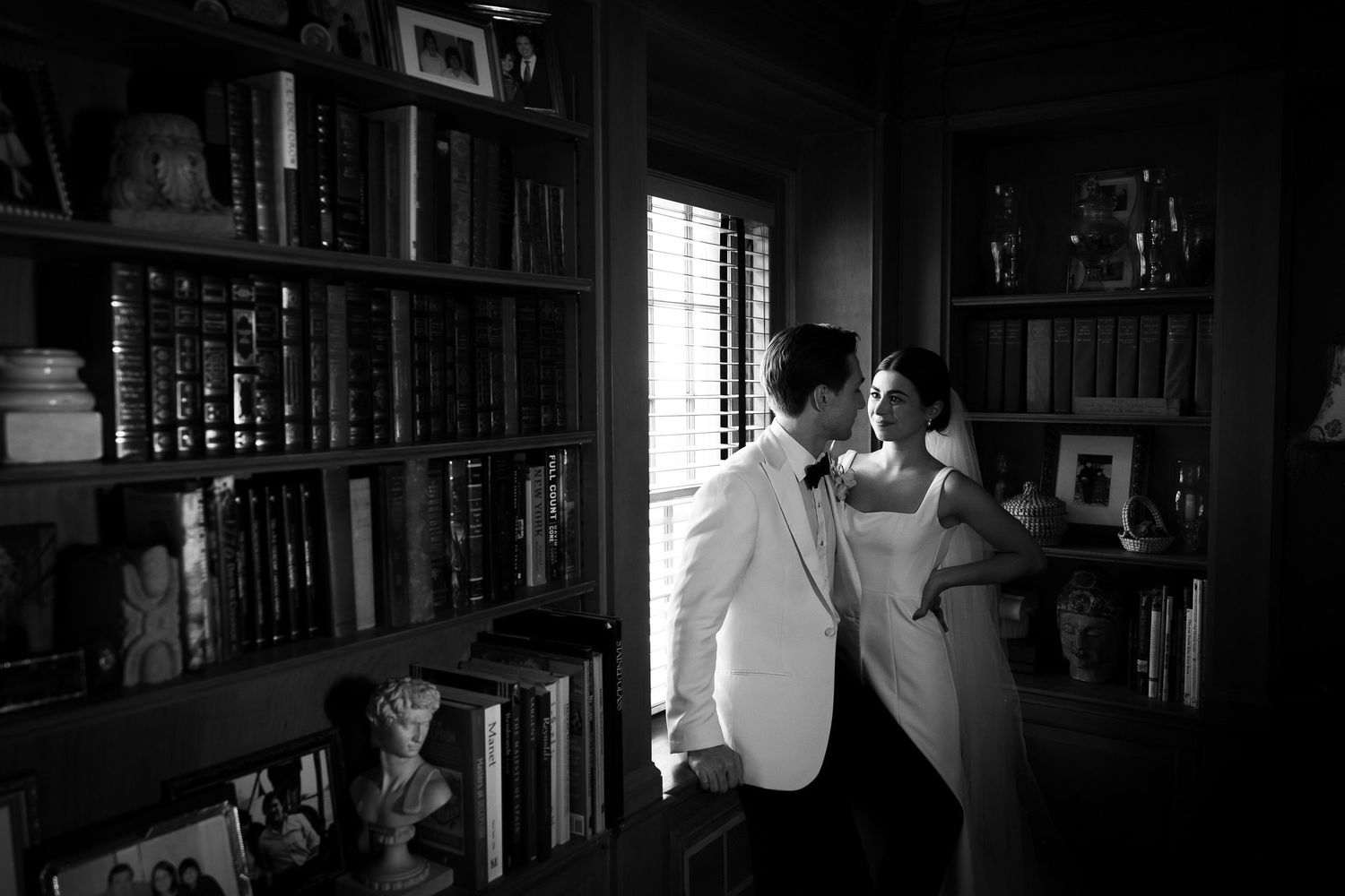 A romantic black and white wedding photo in a library setting with natural window light.