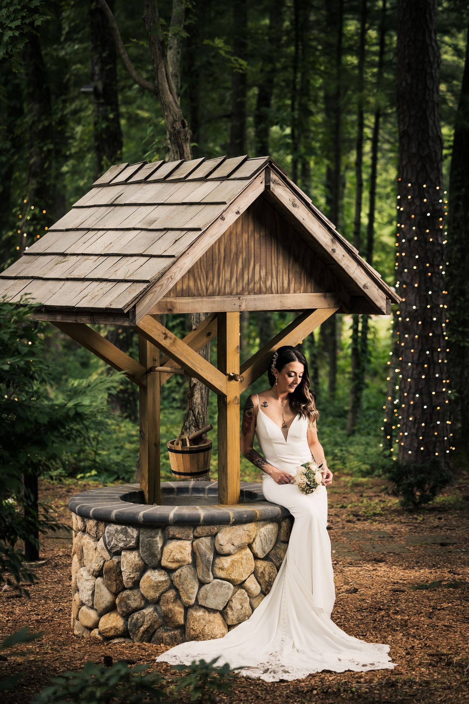 A rustic stone wishing well with a wooden roof surrounded by lush forest creates a magical backdrop for a photoshoot.