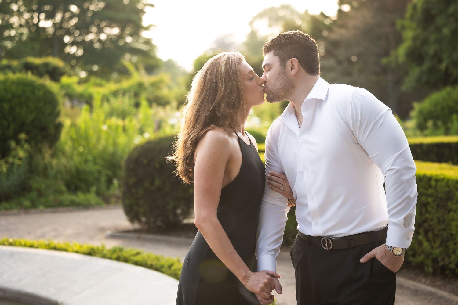 A romantic couple embraces in a sunlit garden setting during a golden hour photoshoot.