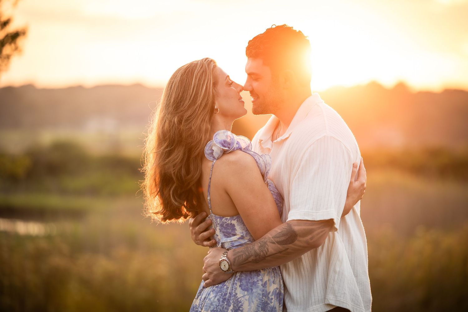 Romantic couple embraces during golden hour sunset in a grassy field with warm glowing light.