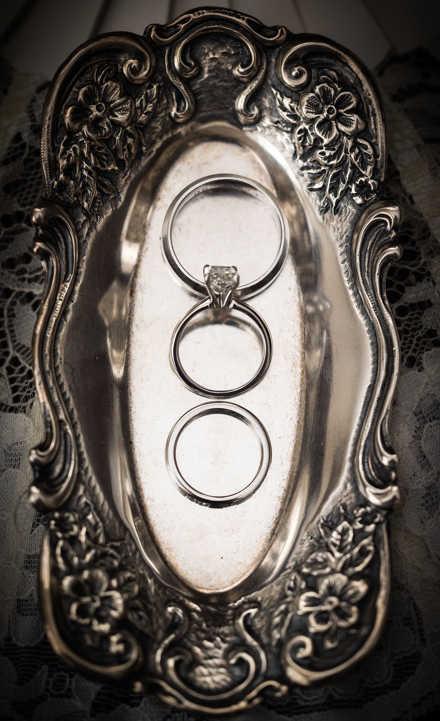 Wedding rings photographed on ornate silver plates with decorative vintage patterns and designs.