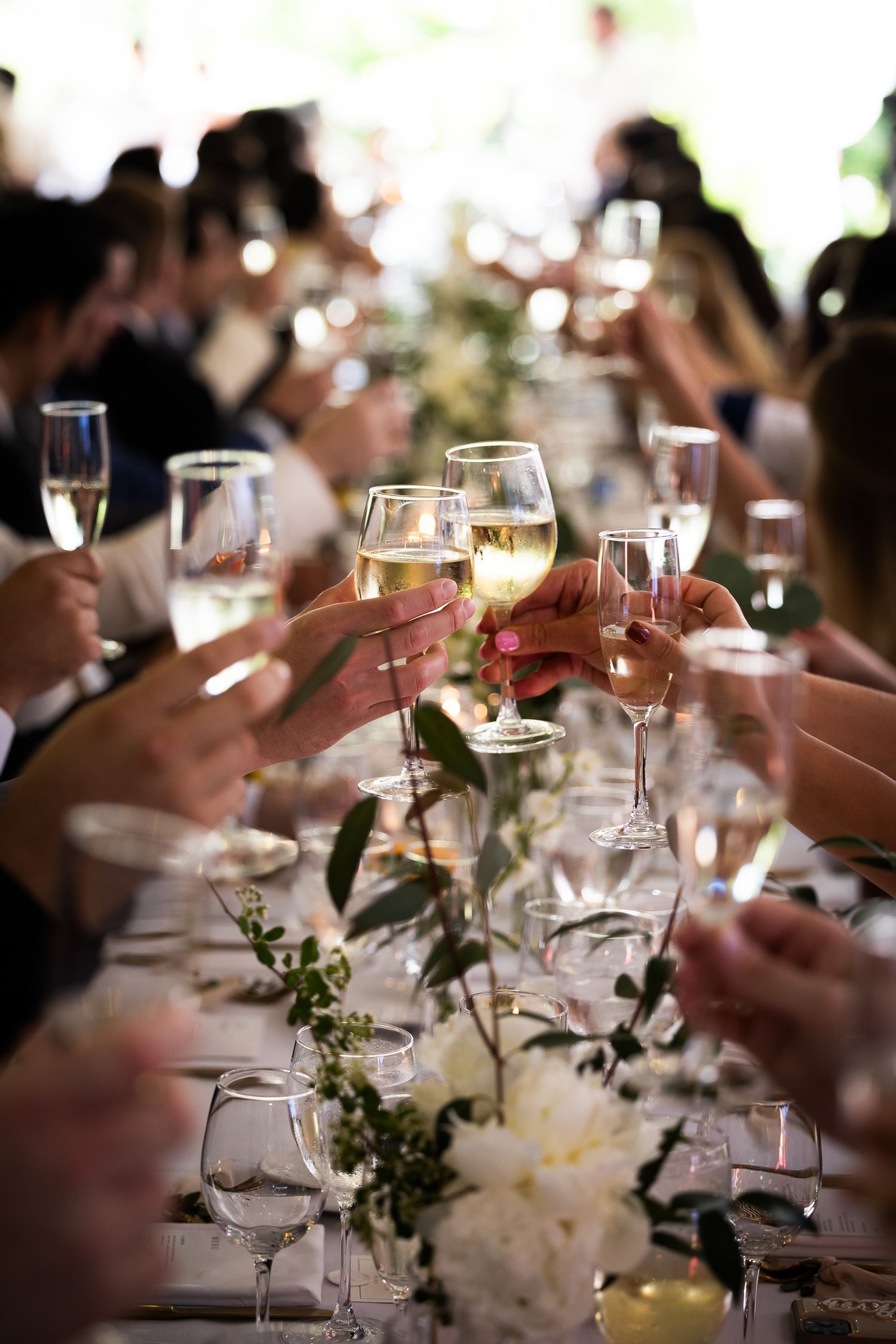 Wedding guests raise glasses in a toast with table decorations and white flowers.