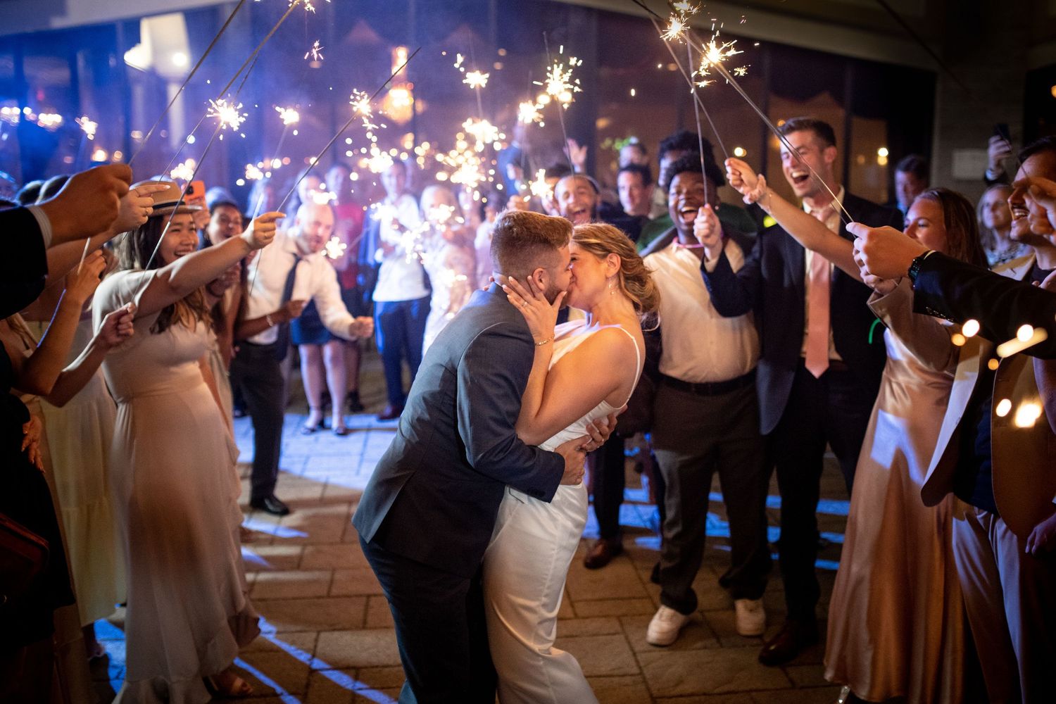 Wedding guests hold sparklers creating a magical light tunnel during an evening celebration.