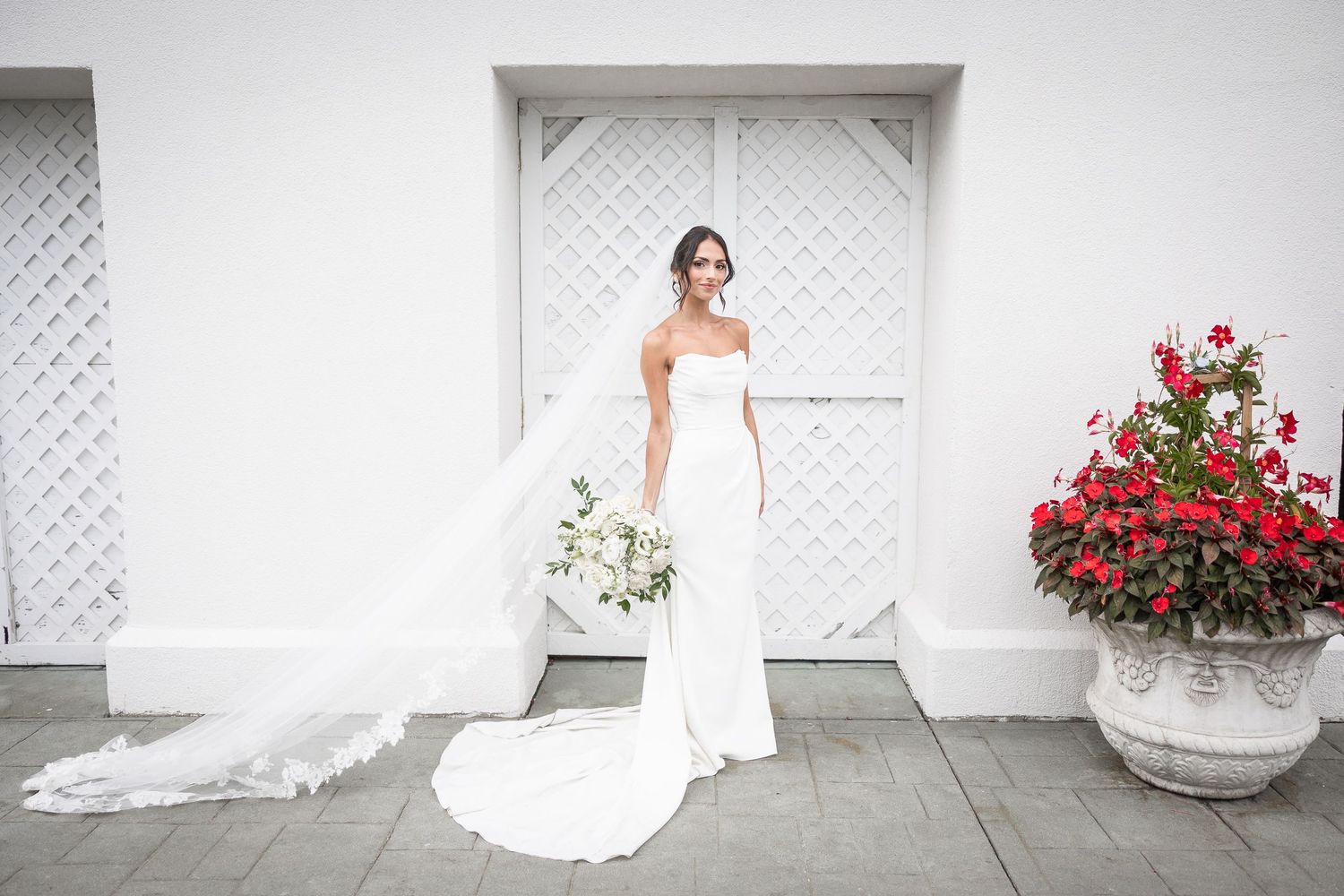 Classic bridal portraits against white lattice wall with red flower arrangements.