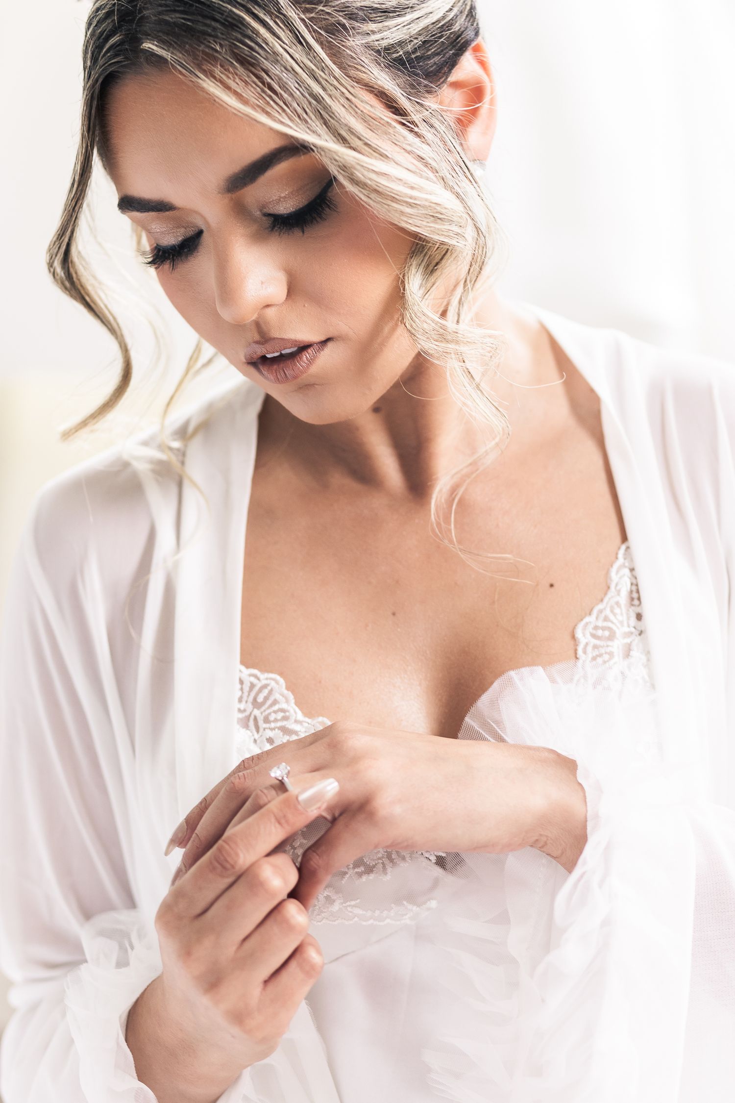 Bride in white robe examines jewelry during wedding preparation.