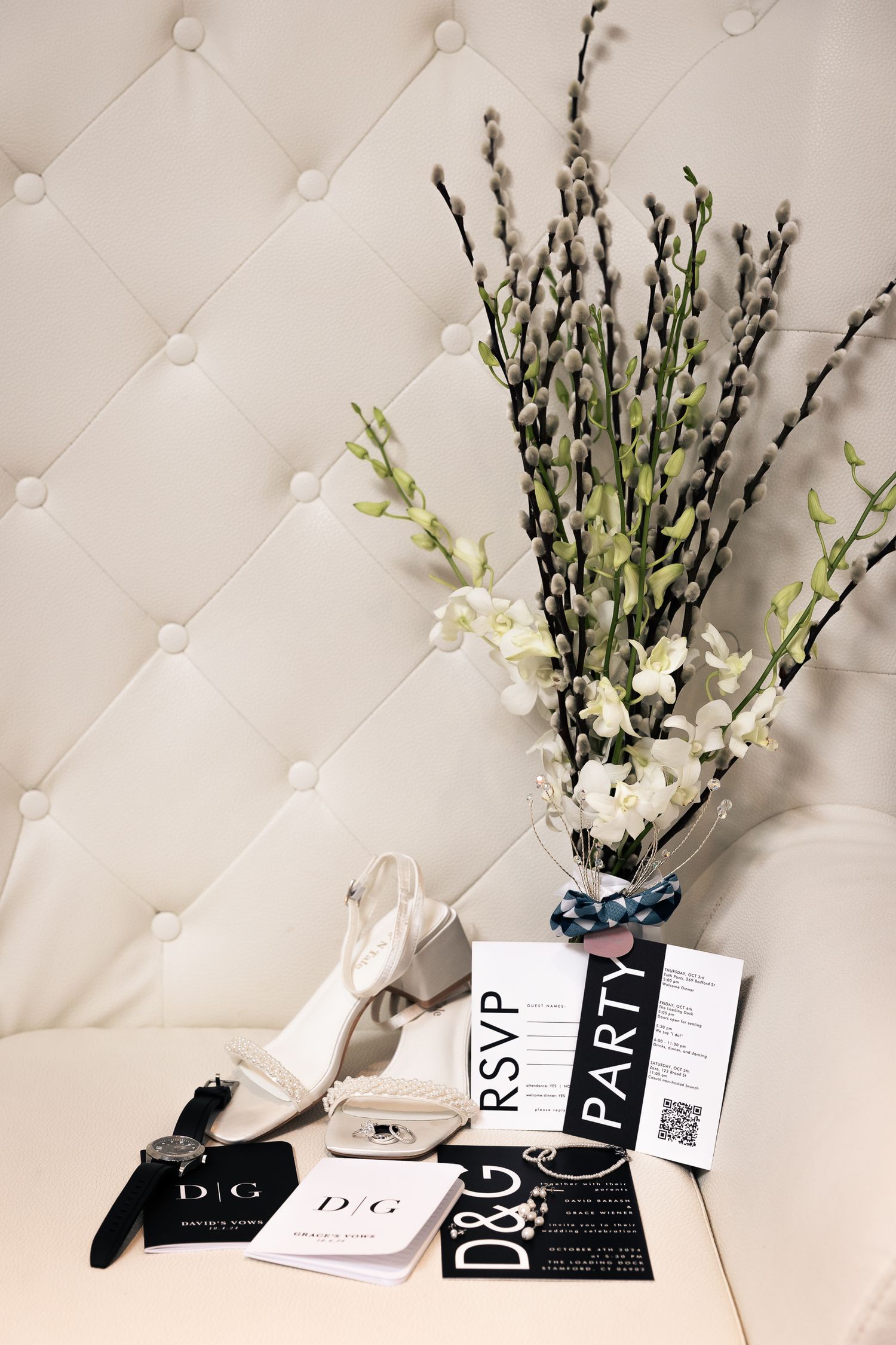 White floral arrangement with tall stems and business cards displayed against a tufted white backdrop.