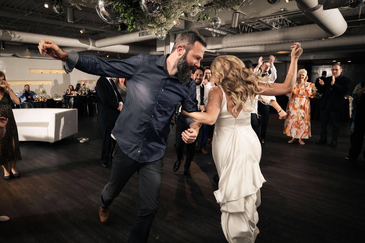 Wedding guests dancing and celebrating on a dimly lit dance floor at a reception party.