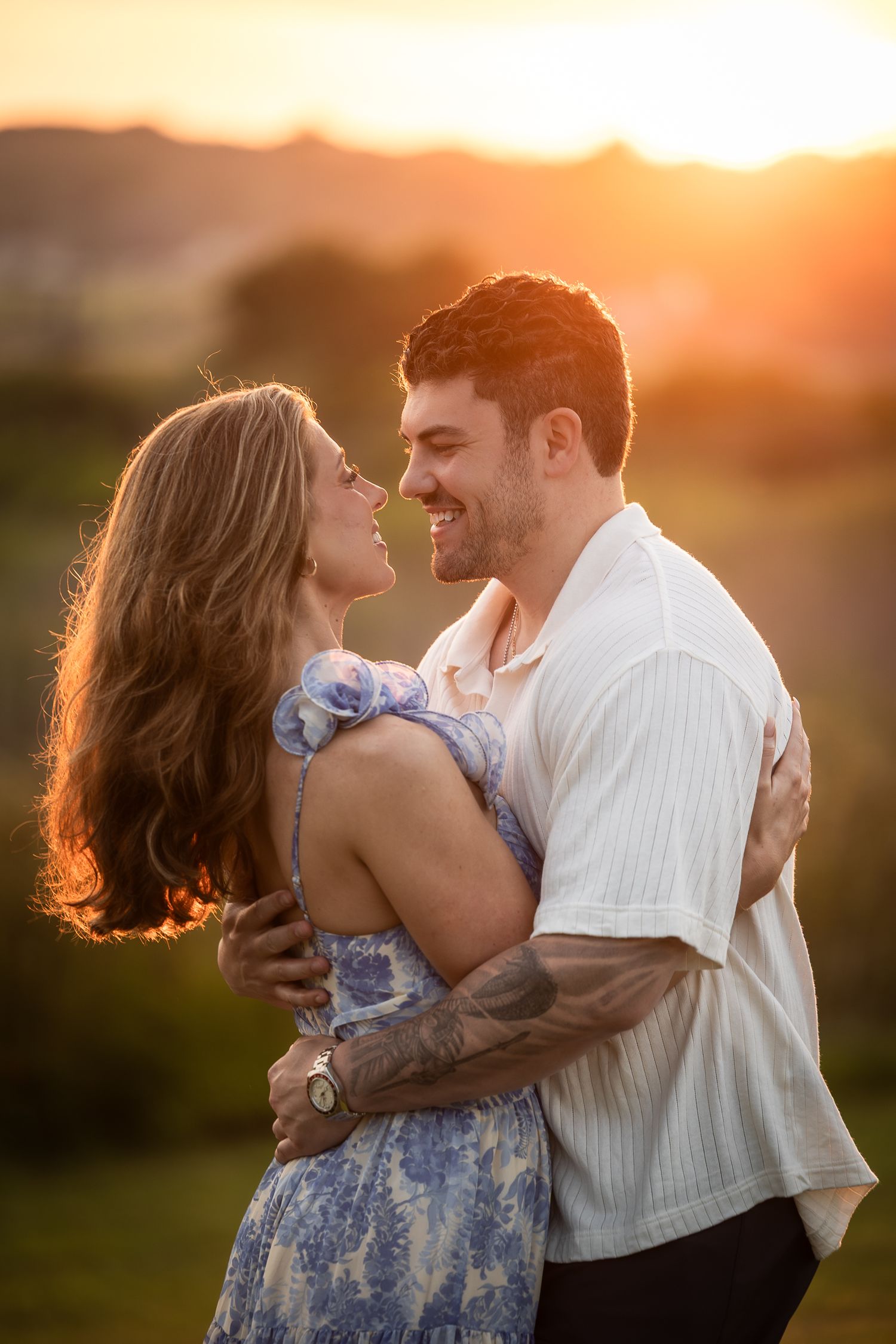 A romantic couple dances together in a sun-drenched field at golden hour, her blue floral dress swaying with the movement.