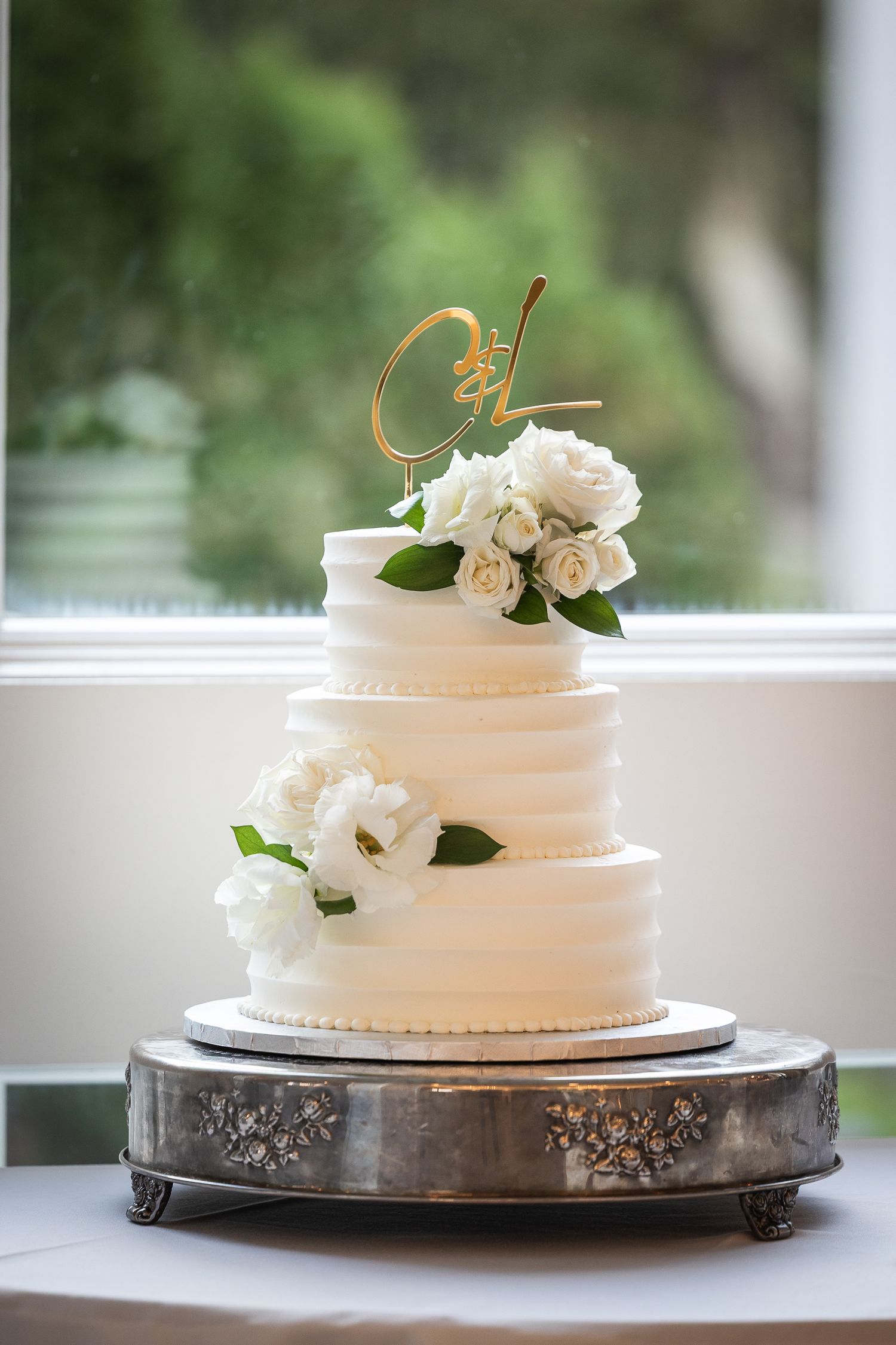 Elegant white wedding cake with simple floral decorations displayed on silver platter.