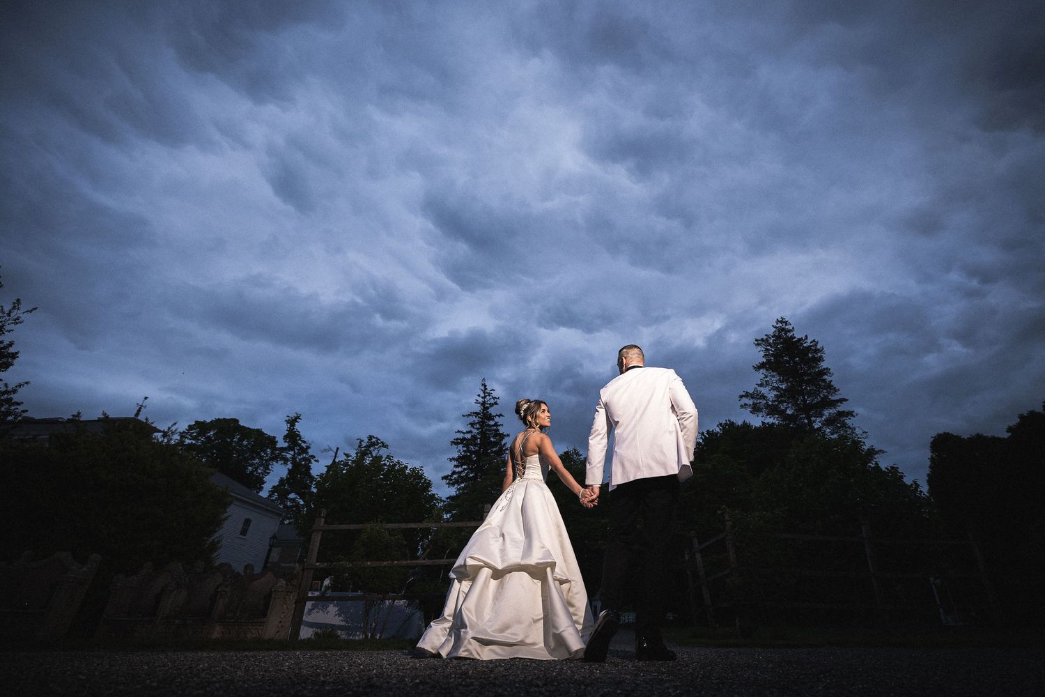 Wedding couple silhouetted against dramatic stormy sky at dusk.