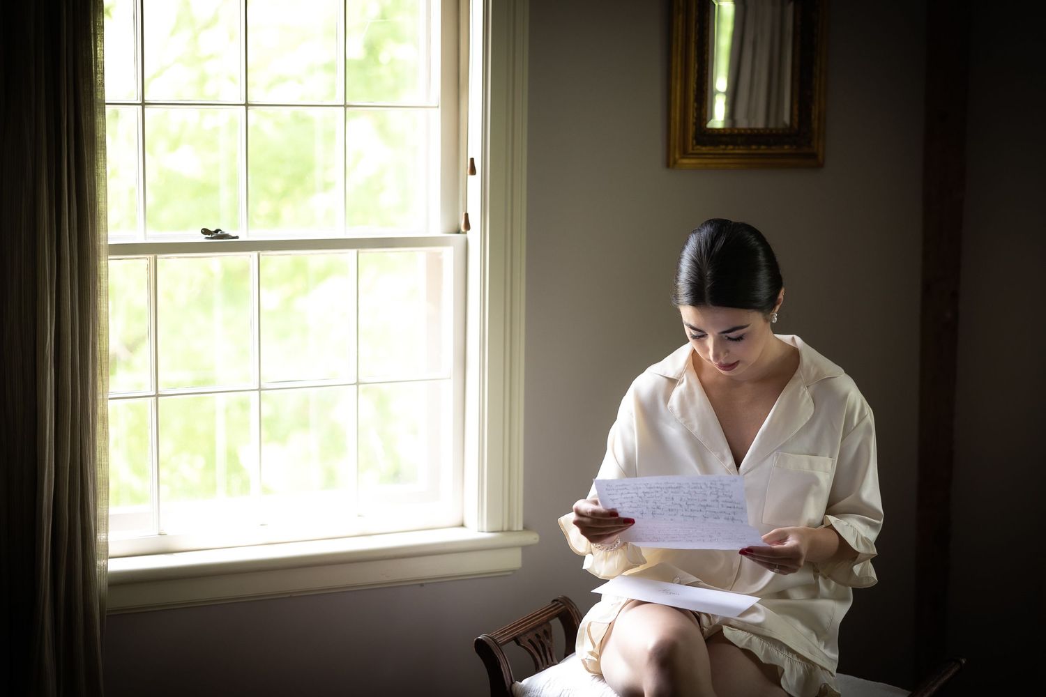 Person reading document near bright window in formal attire.