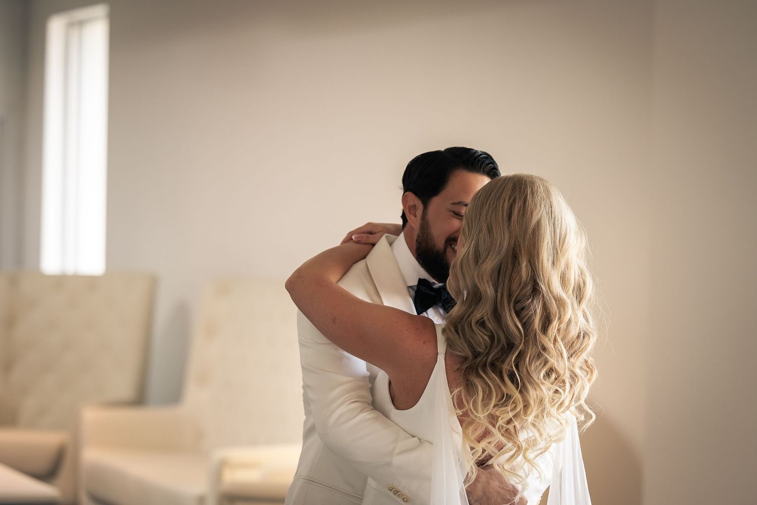 A bride and groom share a romantic first look moment in a sunlit room with neutral tones.