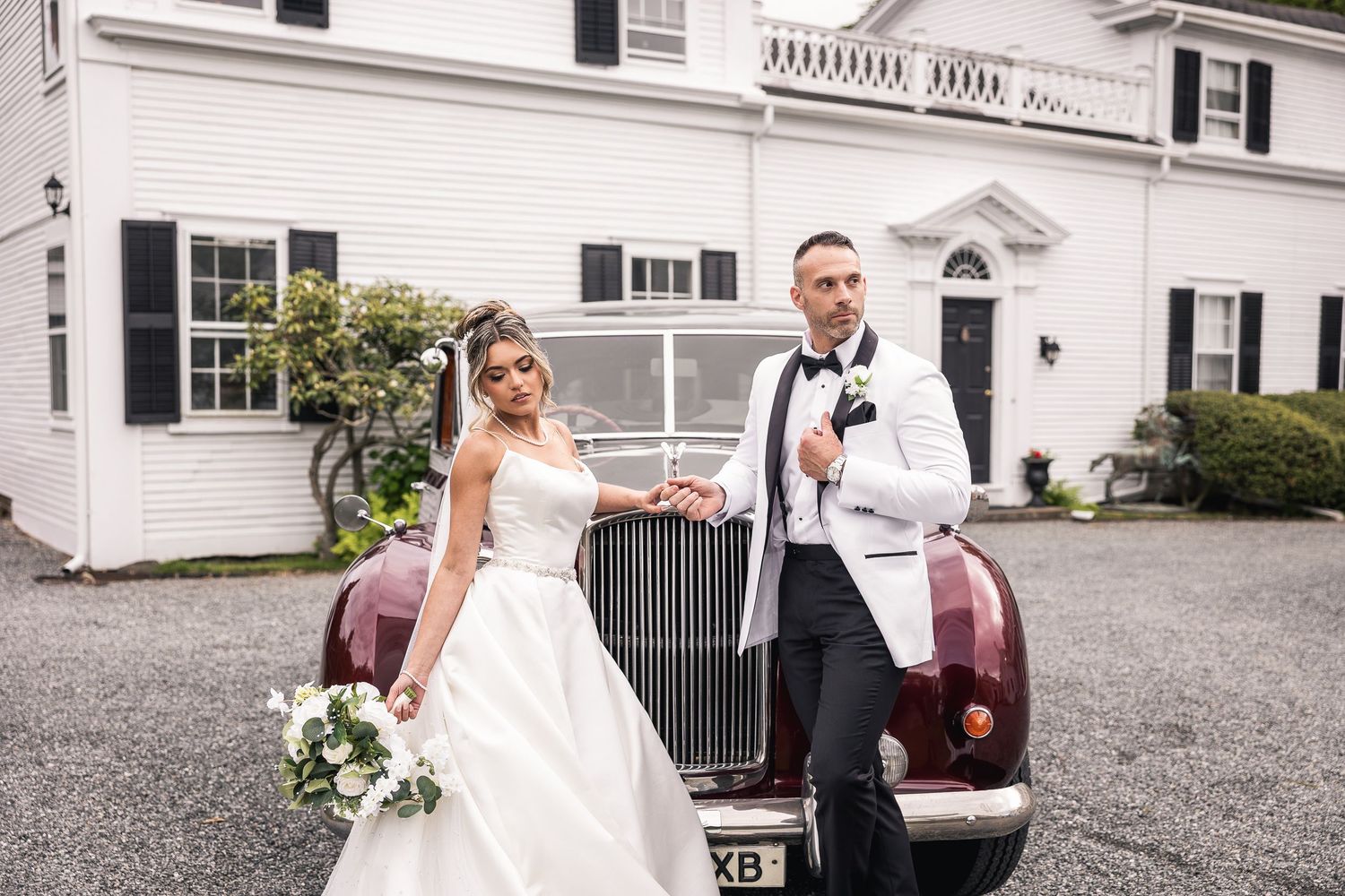 A classic vintage car parked outside a white colonial style building for a wedding.