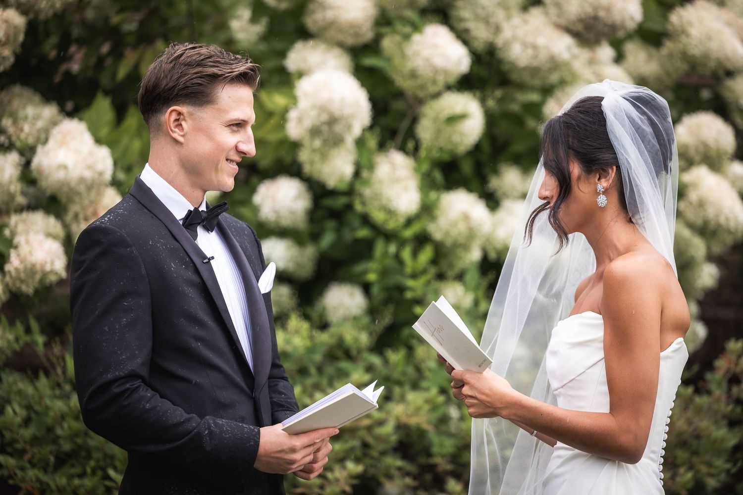 Couple sharing emotional first look moment surrounded by white floral arrangements.