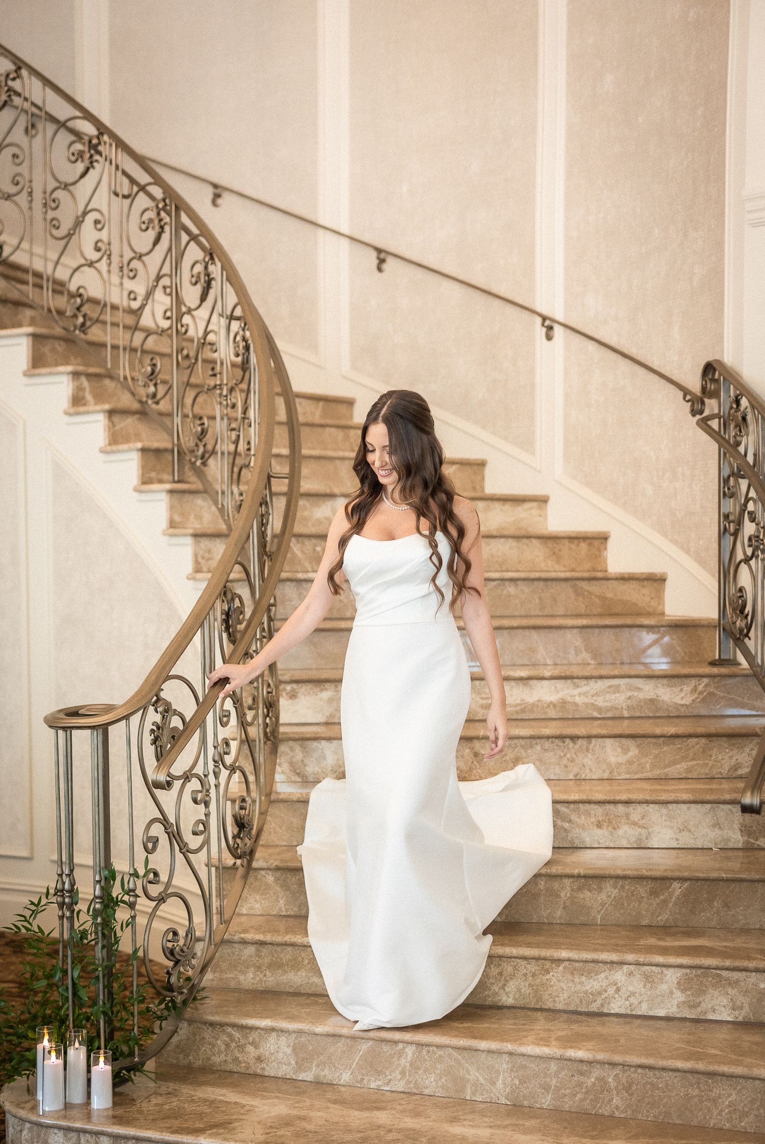 Bride in white dress sitting elegantly on ornate marble staircase with wrought iron railings.