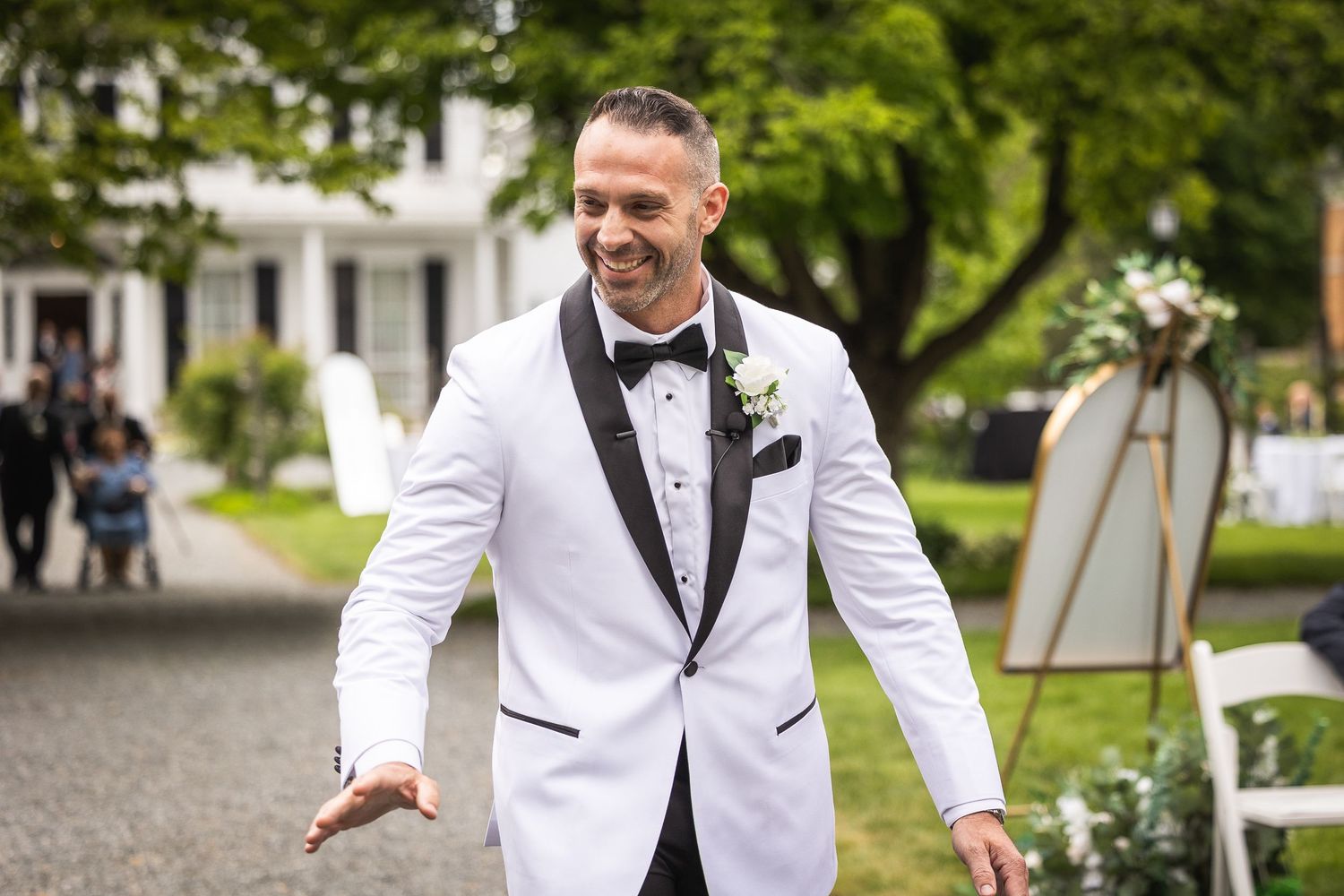 Wedding party members in formal attire pose outdoors on a garden path surrounded by greenery.