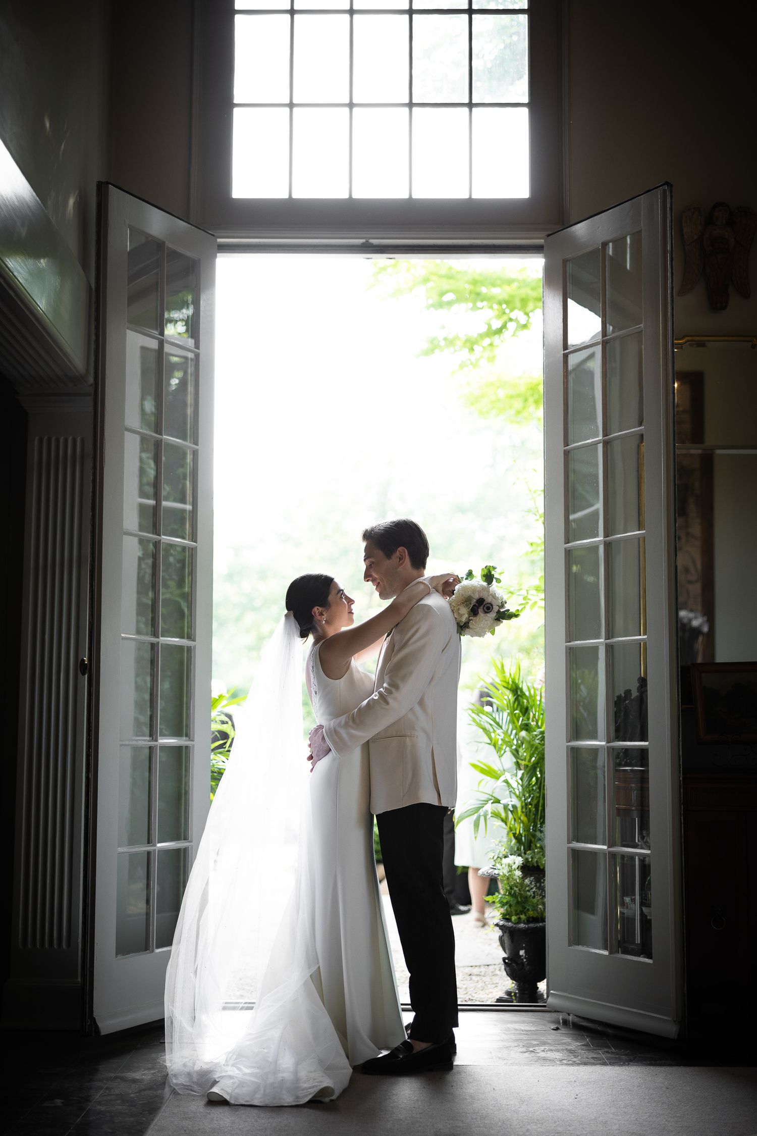 A silhouetted couple embraces in front of bright French doors during their wedding.