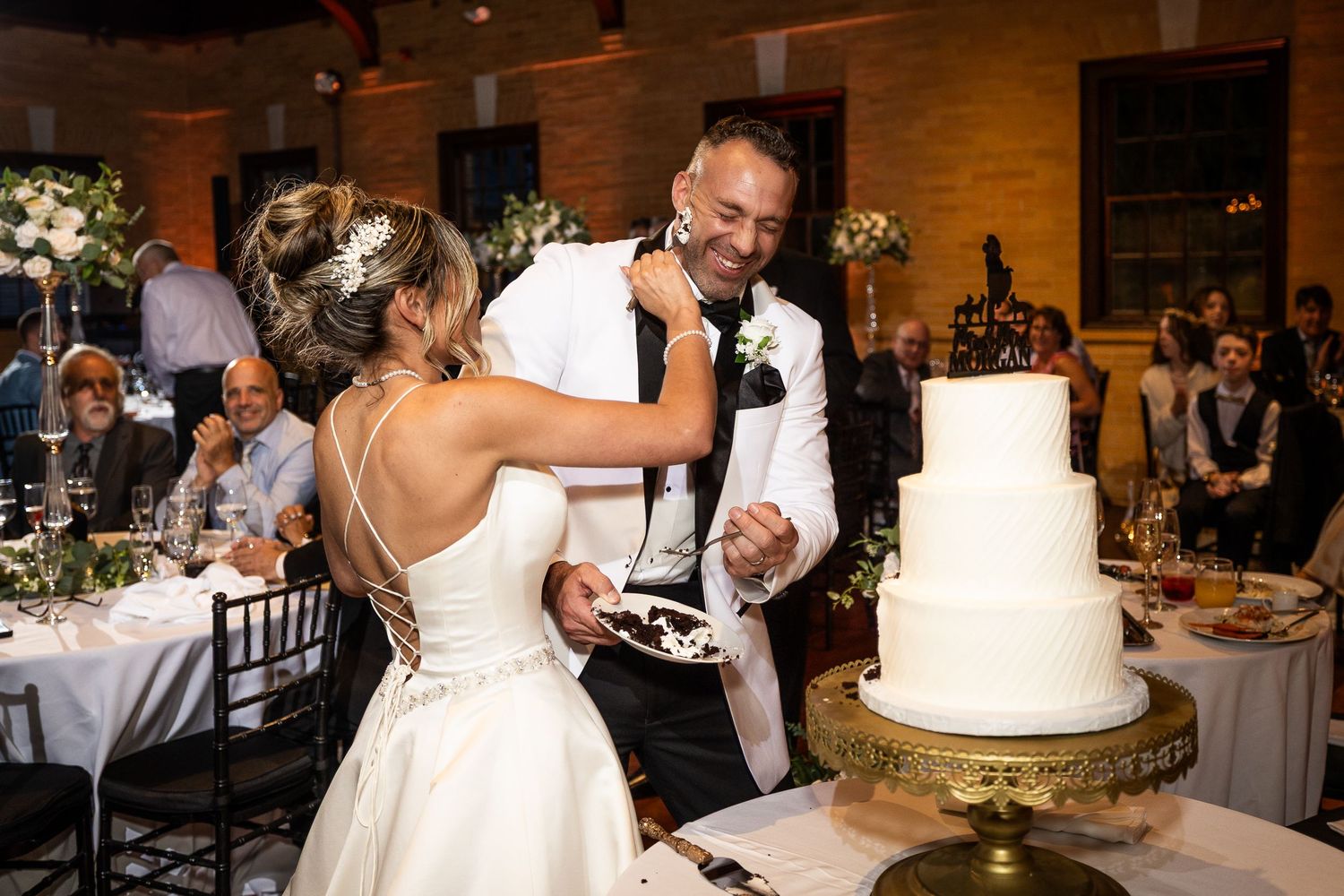 Elegant wedding reception setup with white linens, floral centerpieces, and tiered white cake.