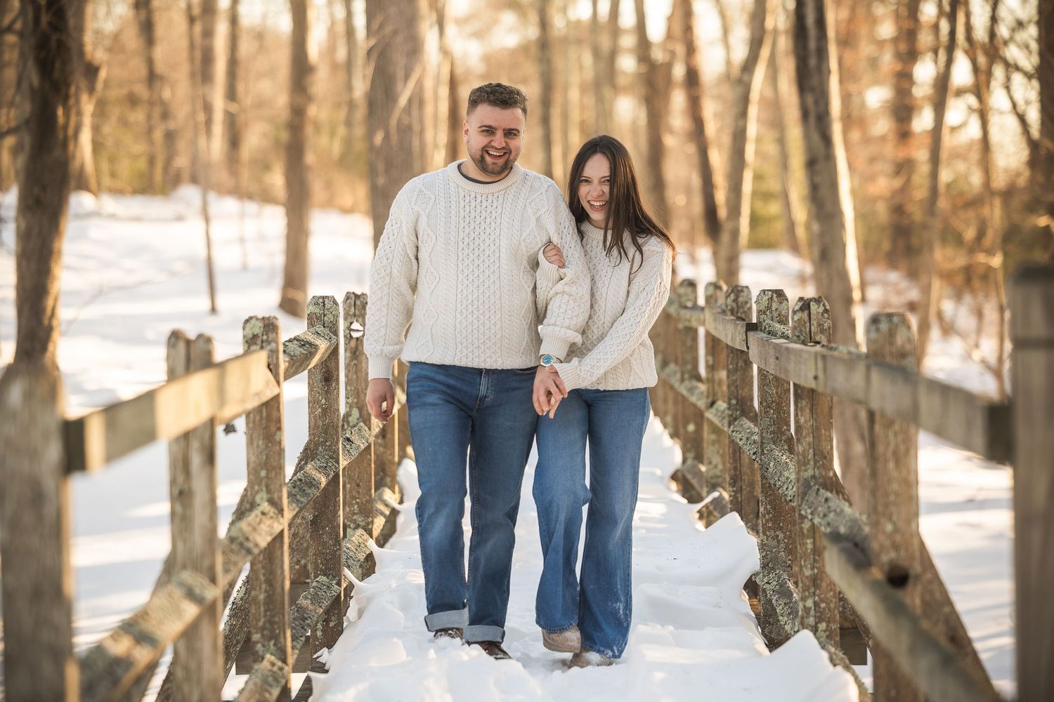 A couple walks together through a snowy forest path holding hands on a winter day.