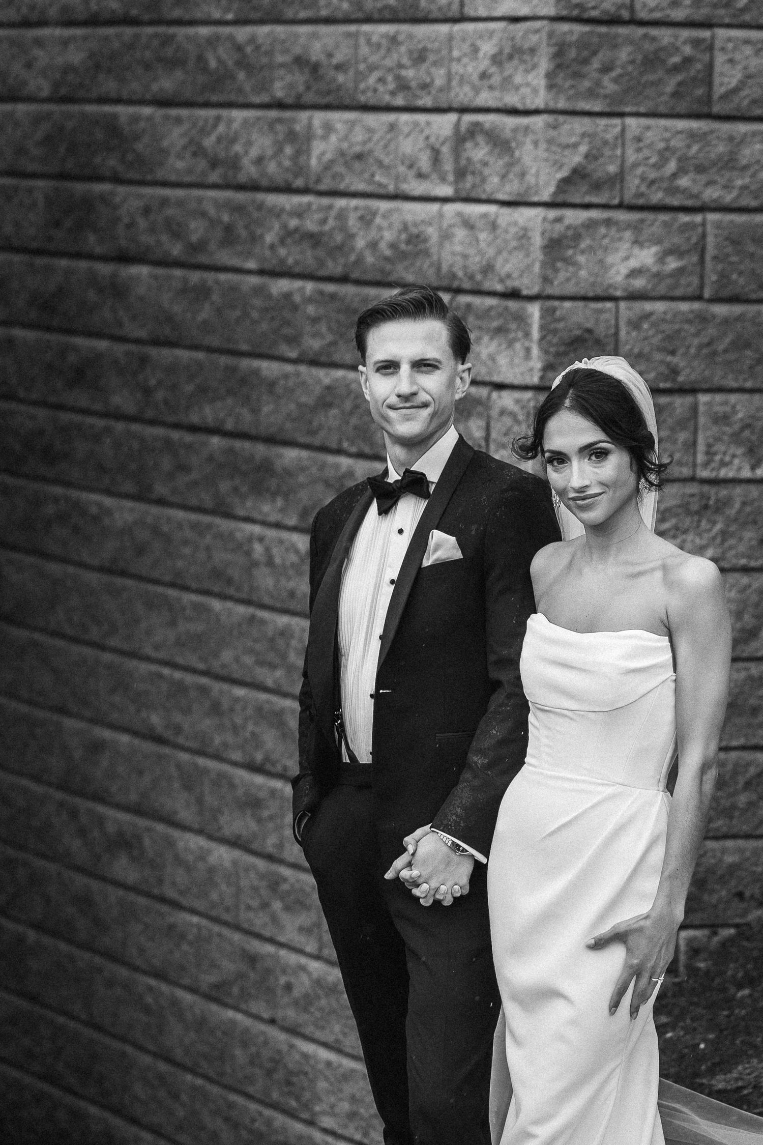 Black and white portrait of newlyweds against textured stone wall background.