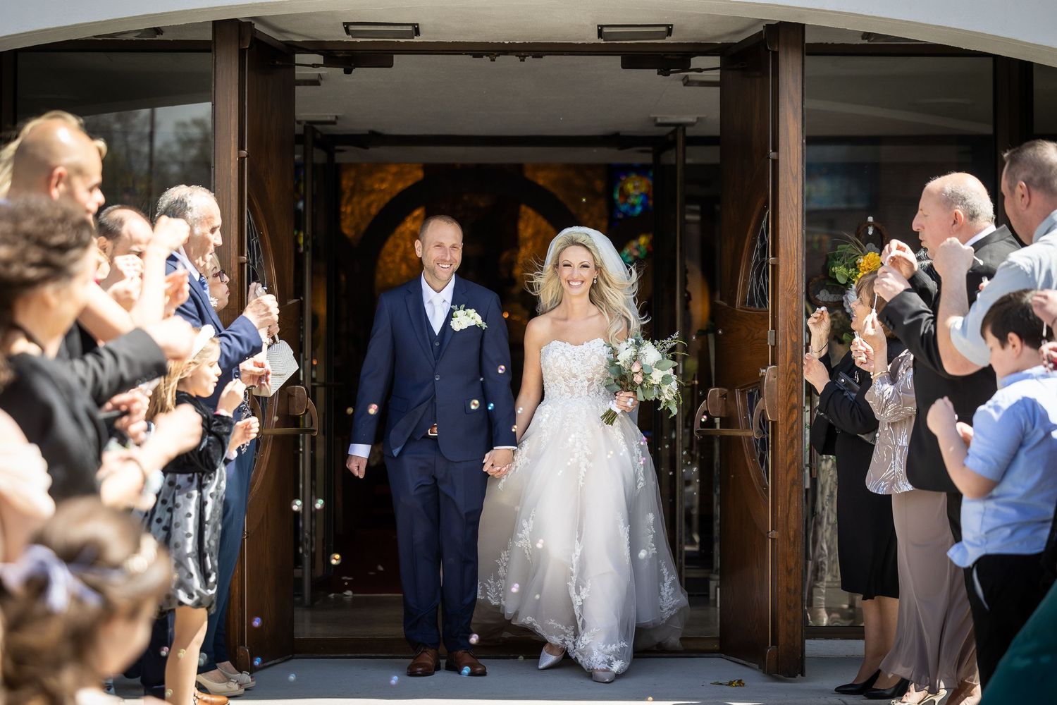 Wedding guests line up outside a rustic wooden venue to celebrate the newlyweds' grand exit.