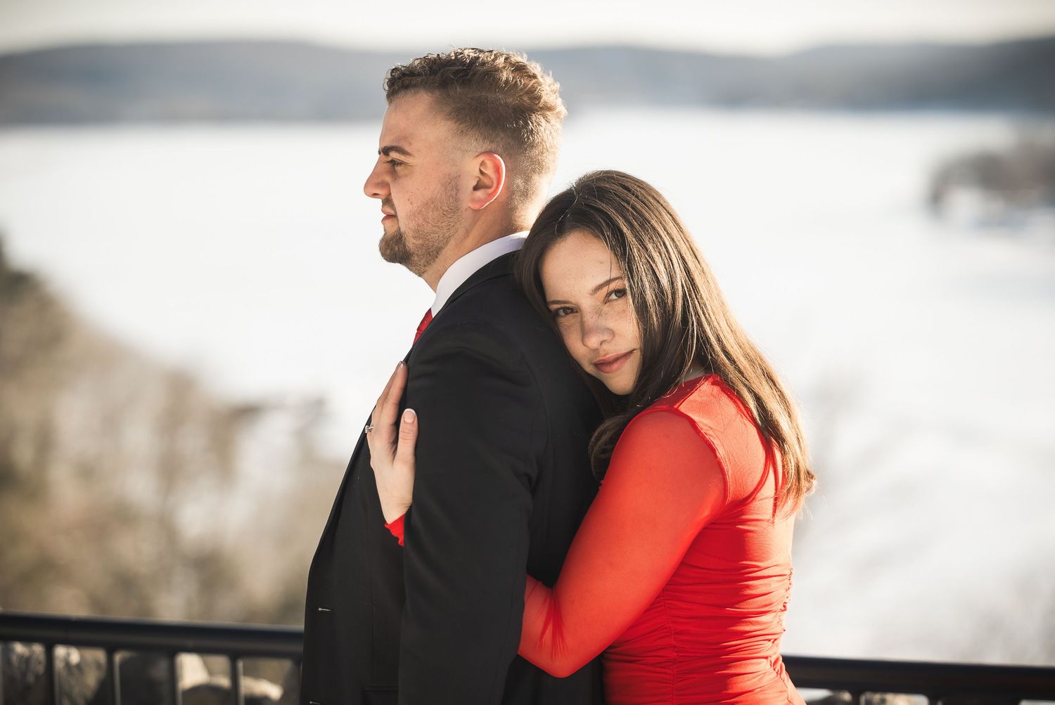 A couple in winter attire embraces outdoors during an intimate photo session with a snowy backdrop.