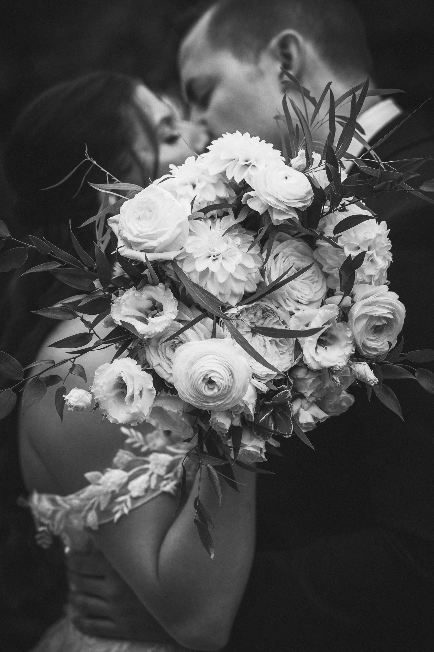 Black and white photo of a romantic moment with white rose bouquet in the foreground.