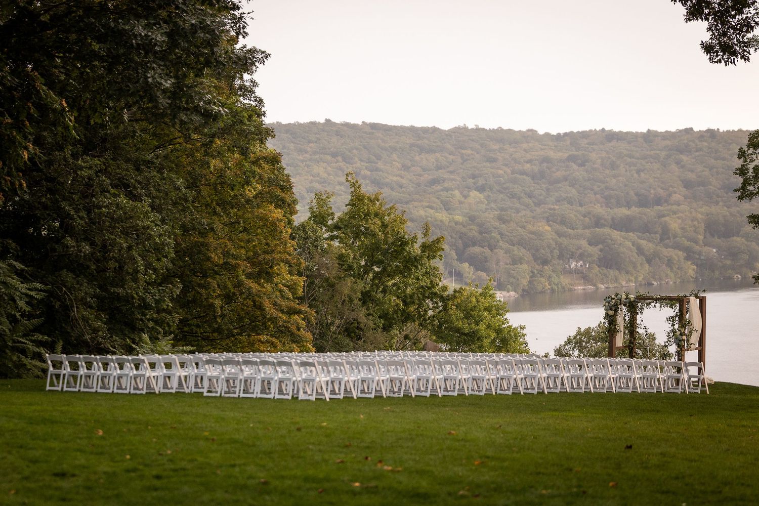 Rows of white chairs set up for an outdoor wedding ceremony overlooking a scenic lake.