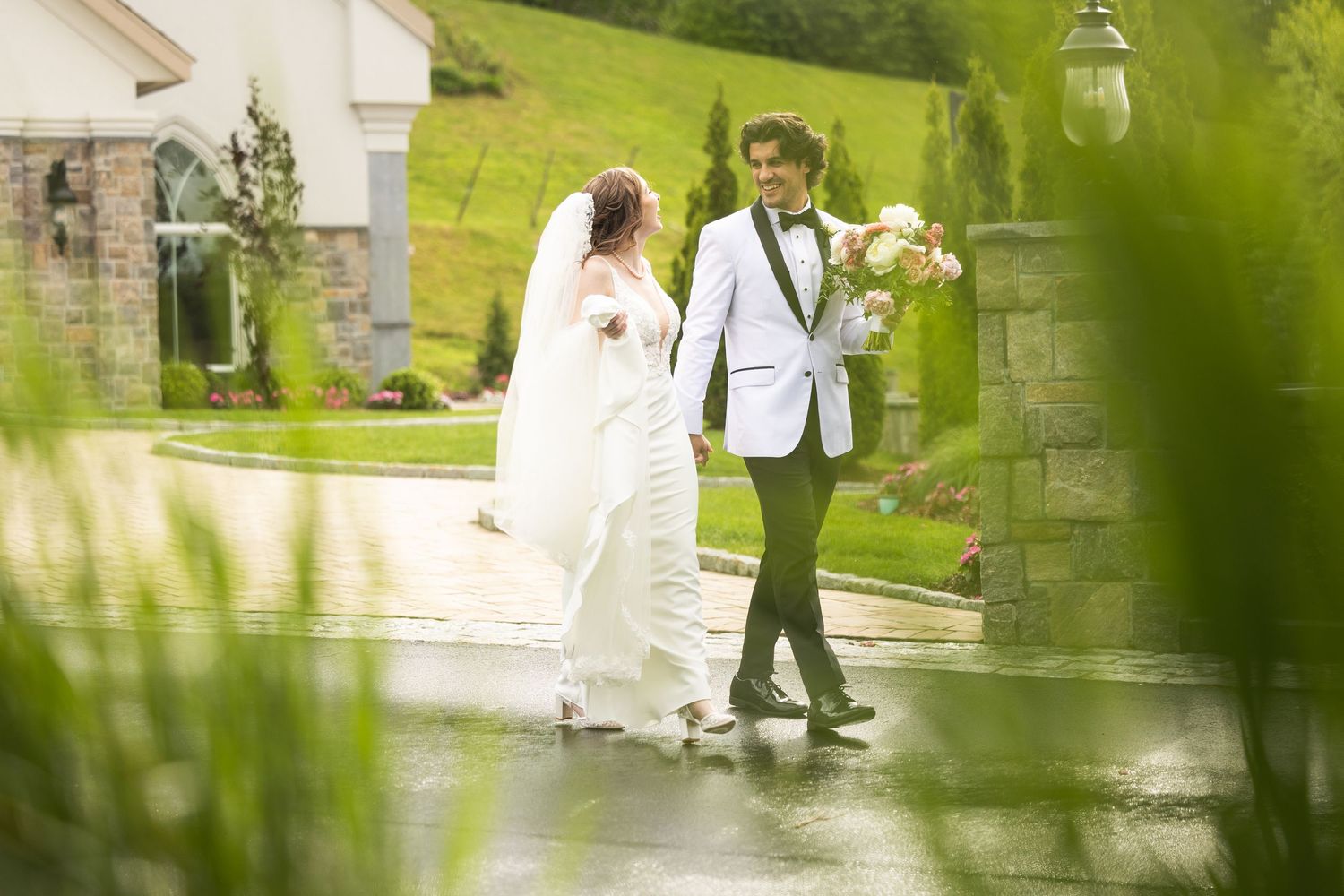 A wedding couple walks along a stone pathway surrounded by lush greenery on their special day.