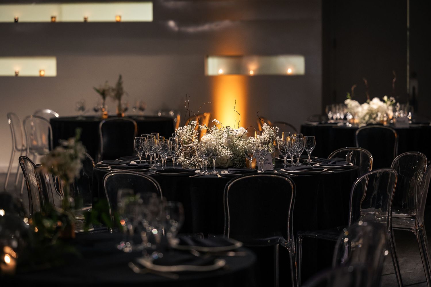 Elegant wedding reception tables with crystal chandeliers, dark decor, and romantic candlelight create a luxurious atmosphere.