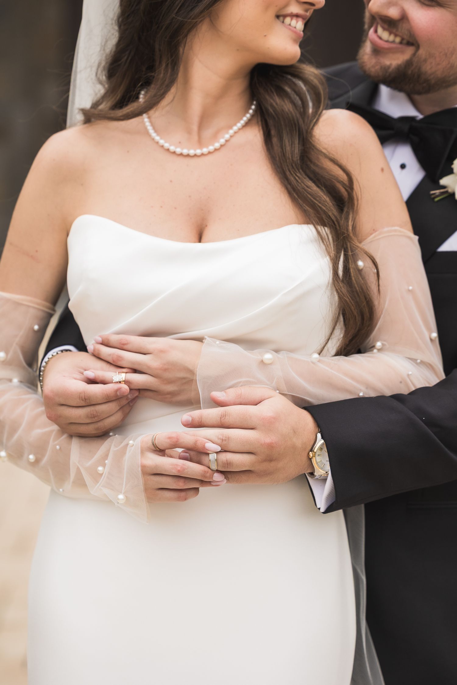 Detail shots of wedding rings and sheer sleeves on a white wedding gown.