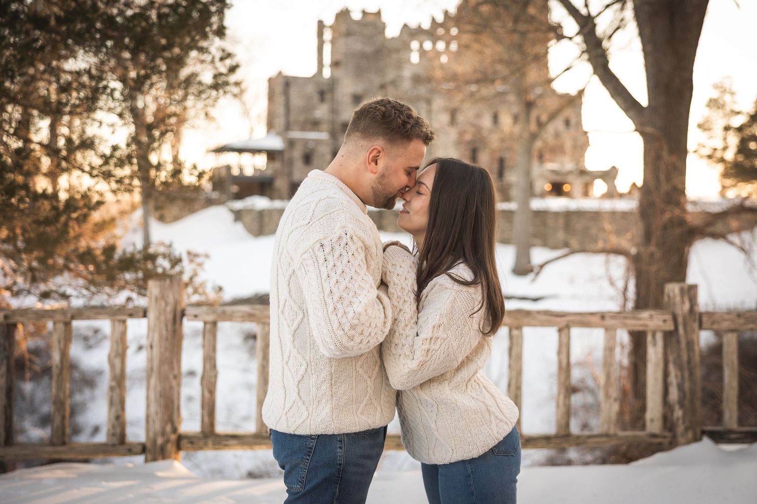 A couple in cozy winter sweaters share romantic moments in a snowy landscape at sunset near stone architecture.