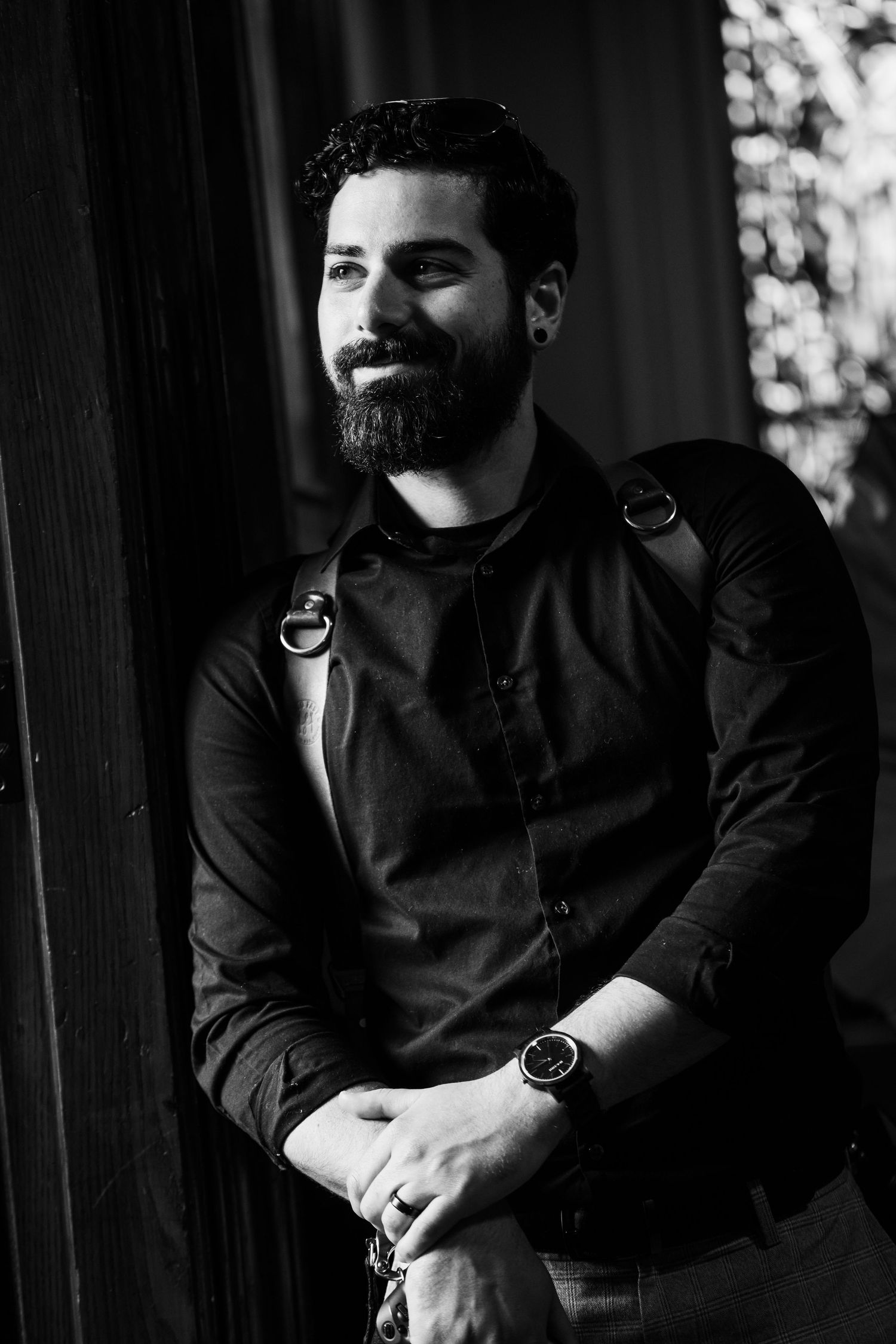 Portrait of a bearded man in black clothing smiling against a dark background.