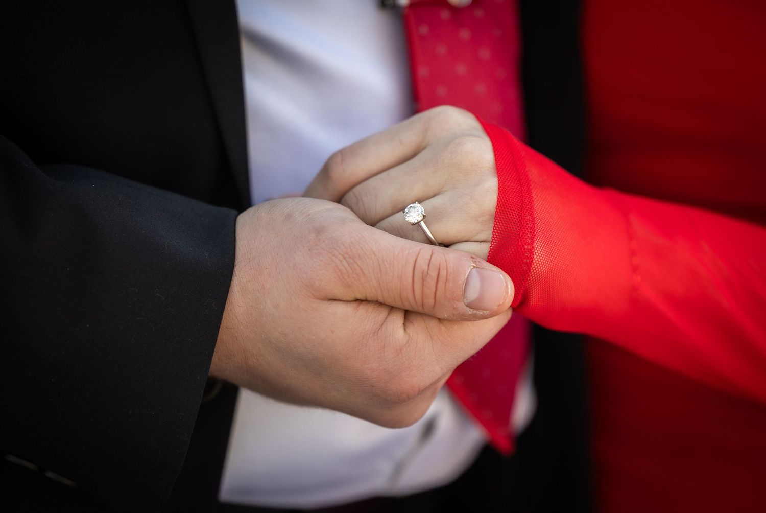 Close-up shot of hands exchanging wedding rings during a ceremony with red background lighting.
