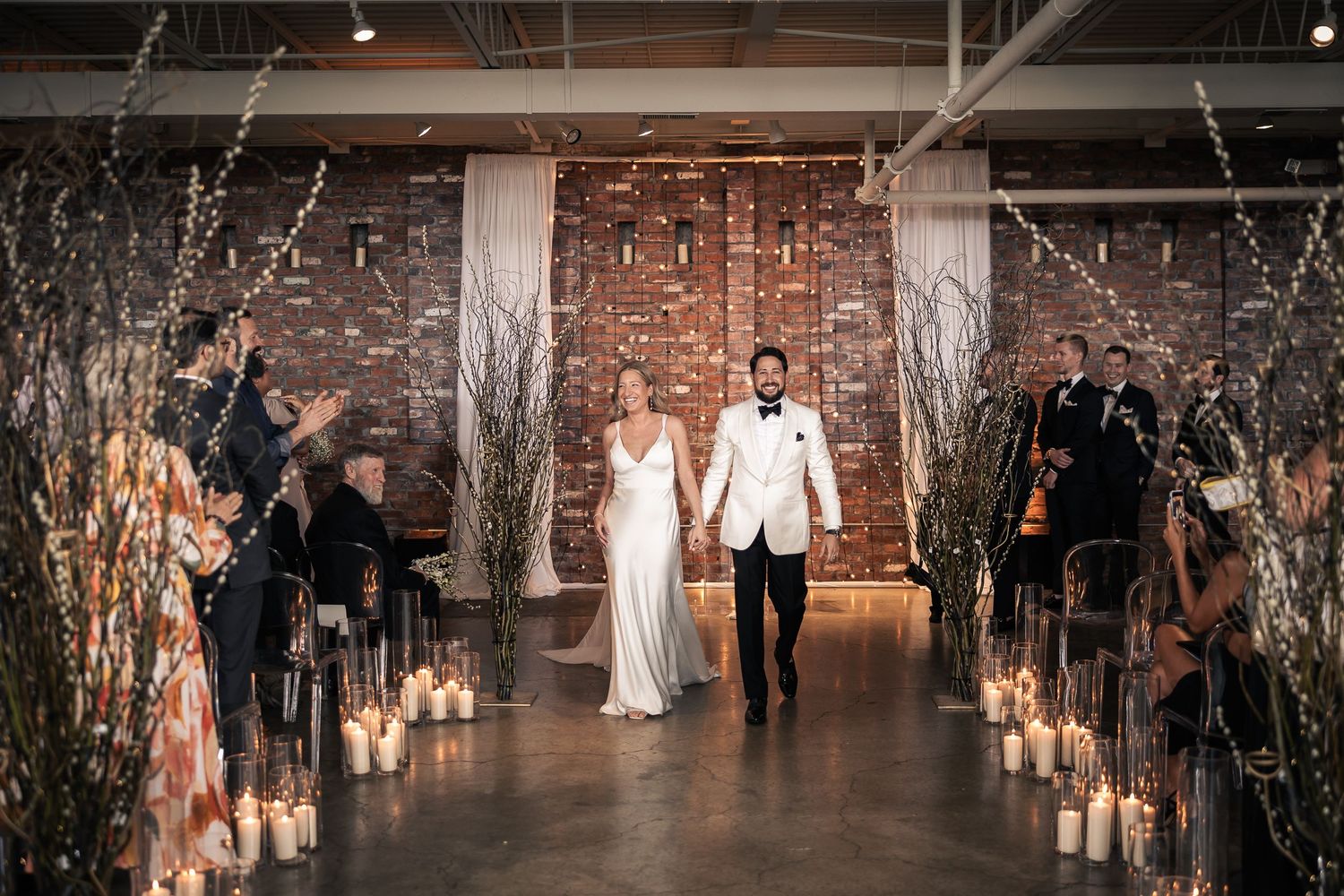 Elegant wedding ceremony setup in an industrial venue with brick walls and illuminated branches creating a romantic atmosphere.