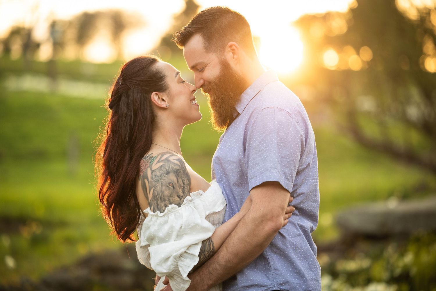 A romantic couple embraces in a sunlit park during golden hour with soft bokeh lighting effects in the background.