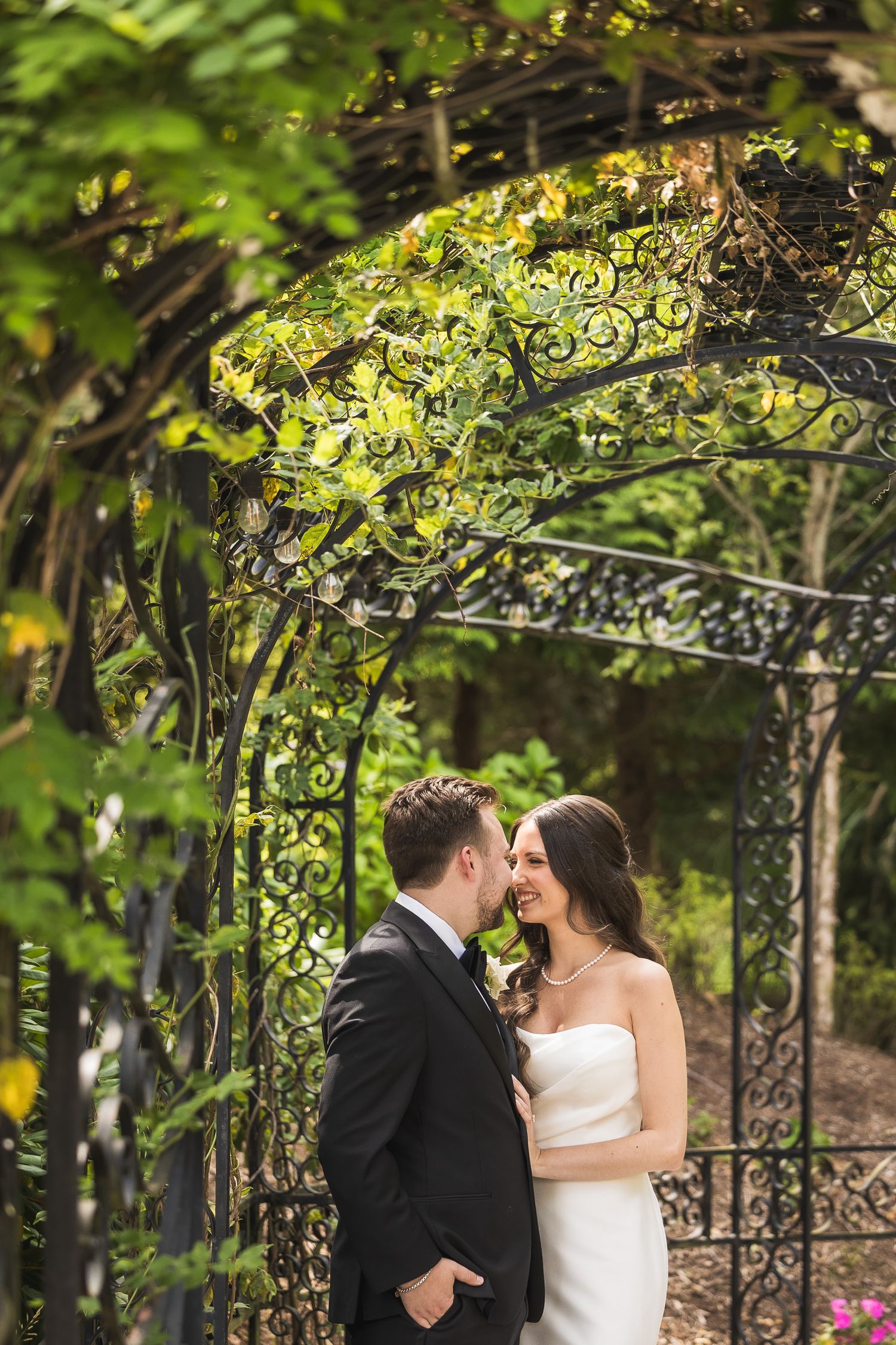 Romantic moment shared under garden arbor with ornate ironwork and lush greenery.