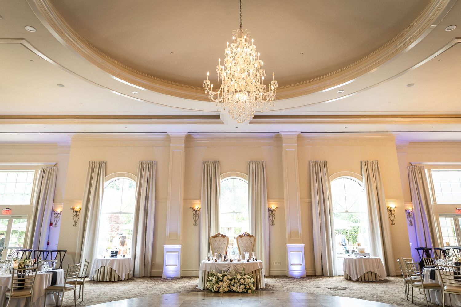 Elegant ballroom with crystal chandeliers and cream-colored walls set up for a wedding reception.