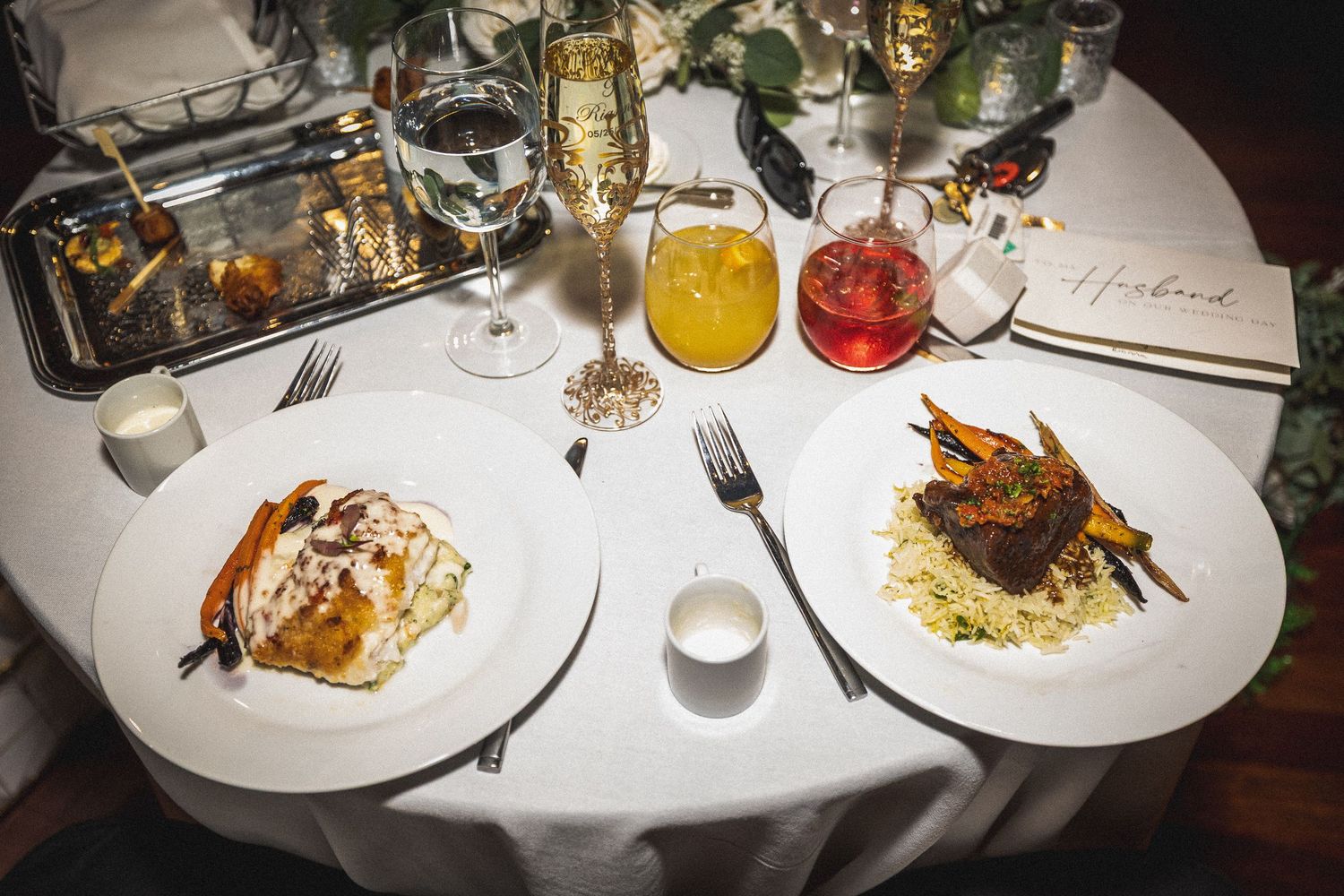 Wedding reception dinner plates with elegant food presentation on white tablecloths.