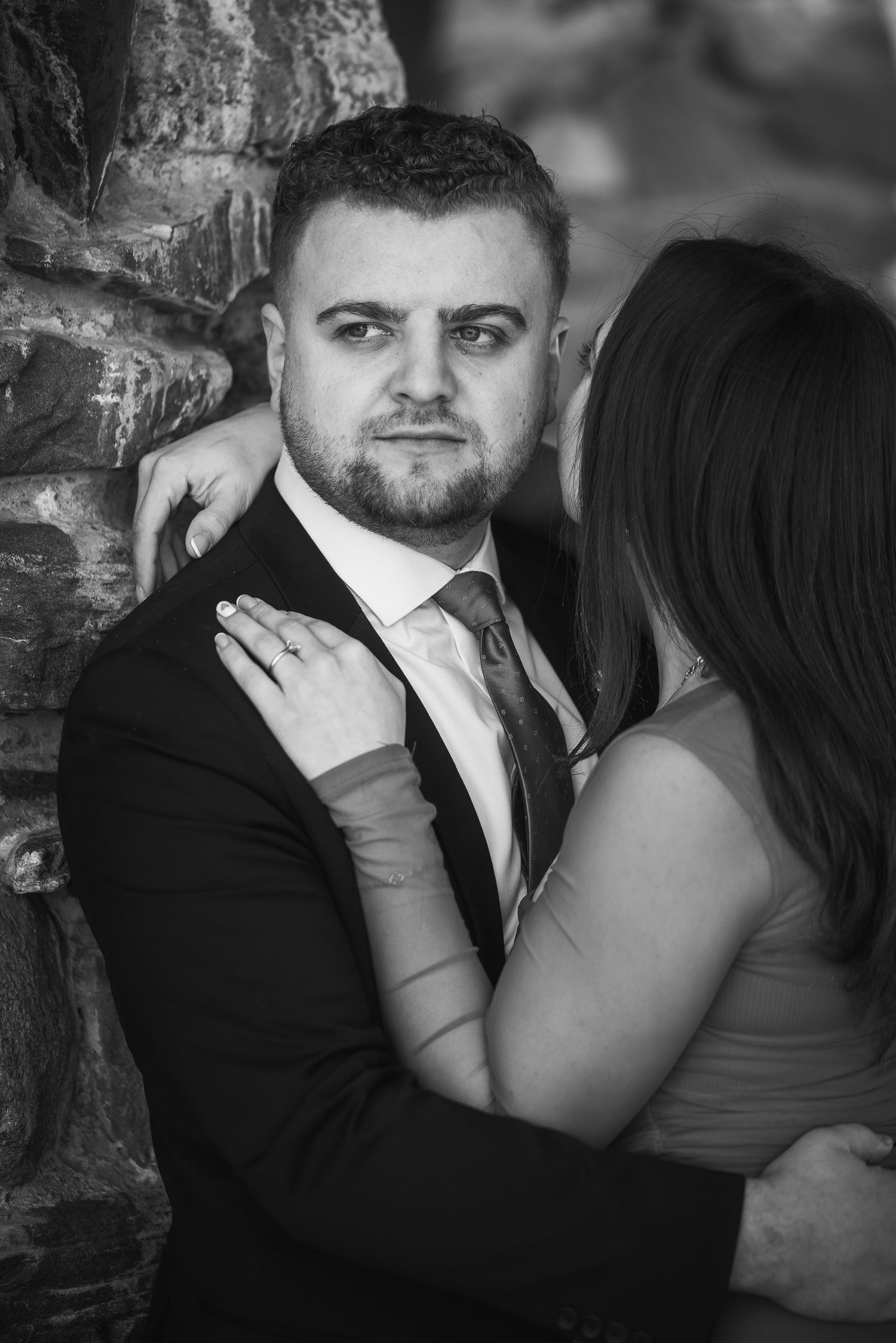 Black and white intimate portrait of a couple embracing against a stone wall during a romantic photoshoot.