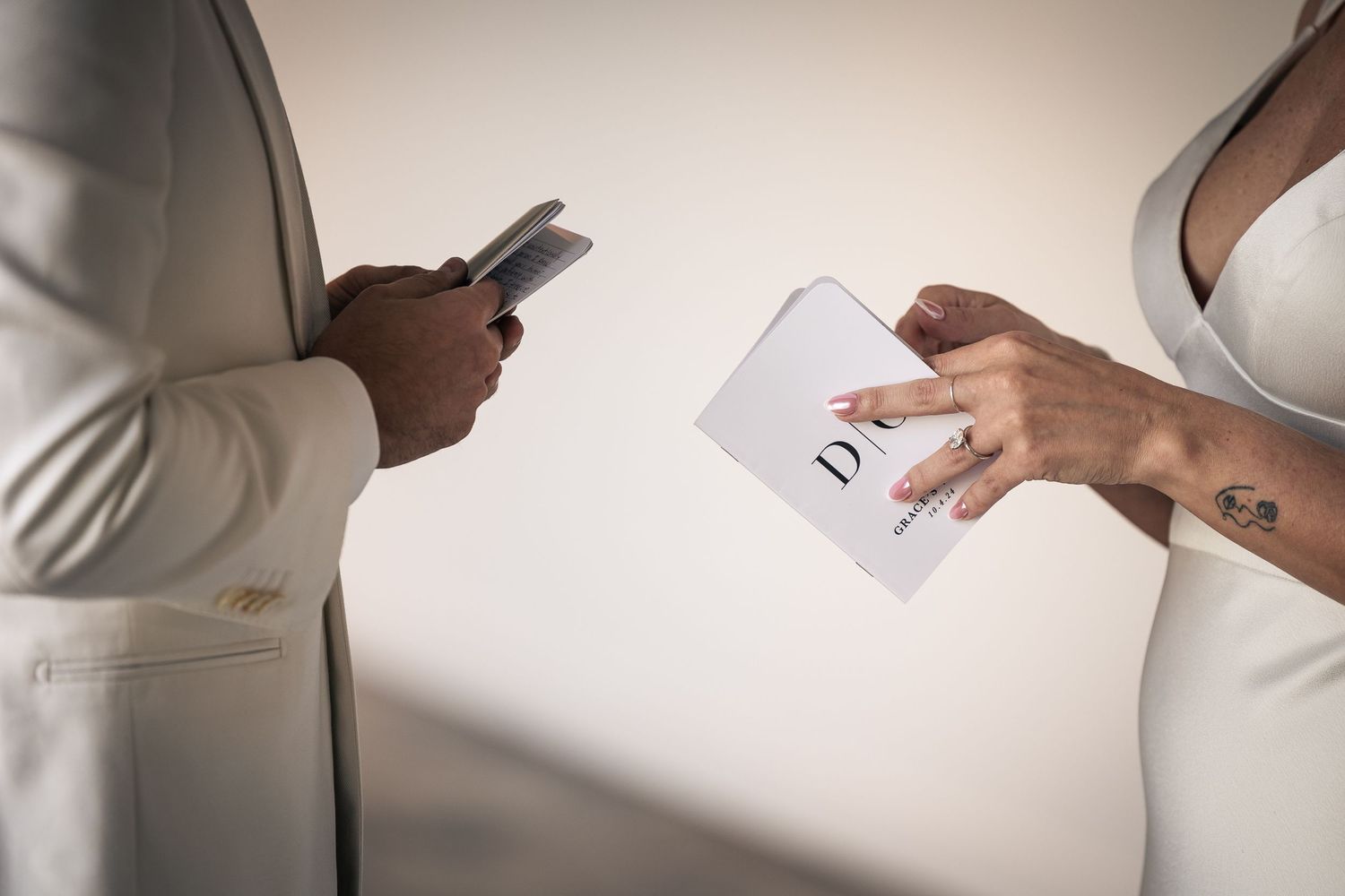 A person in a white blazer holds and signs business documents on a desk with natural lighting.