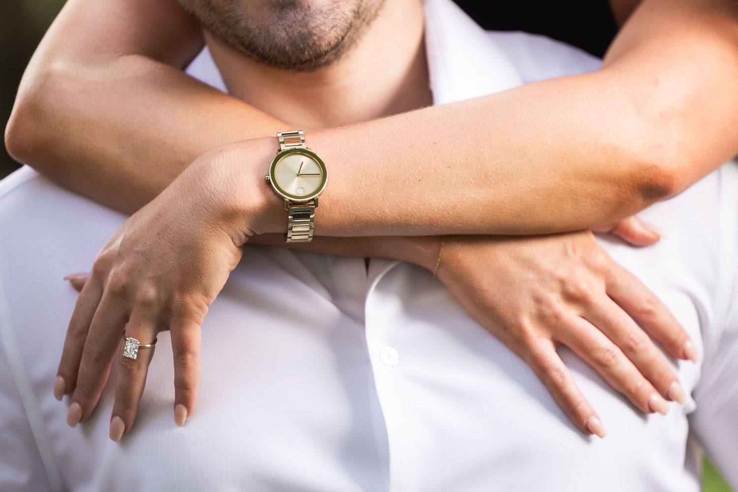 Close-up view of hands resting on white fabric with a gold watch visible on one wrist.