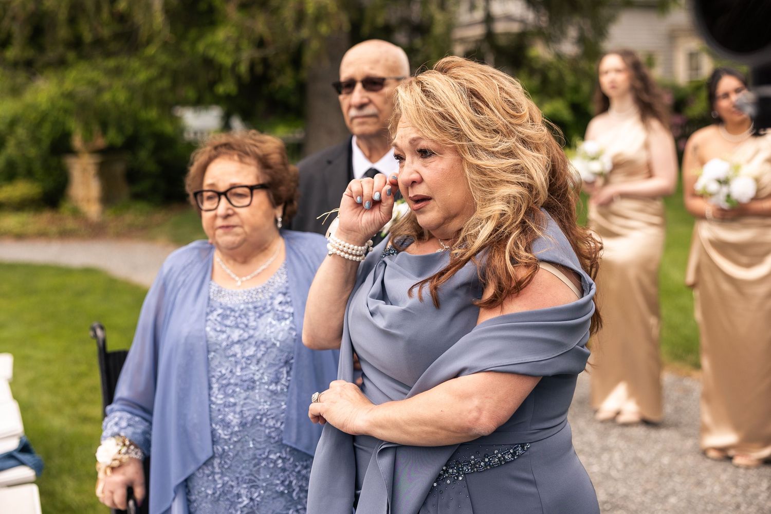 Wedding party members share emotional embraces during outdoor celebration.