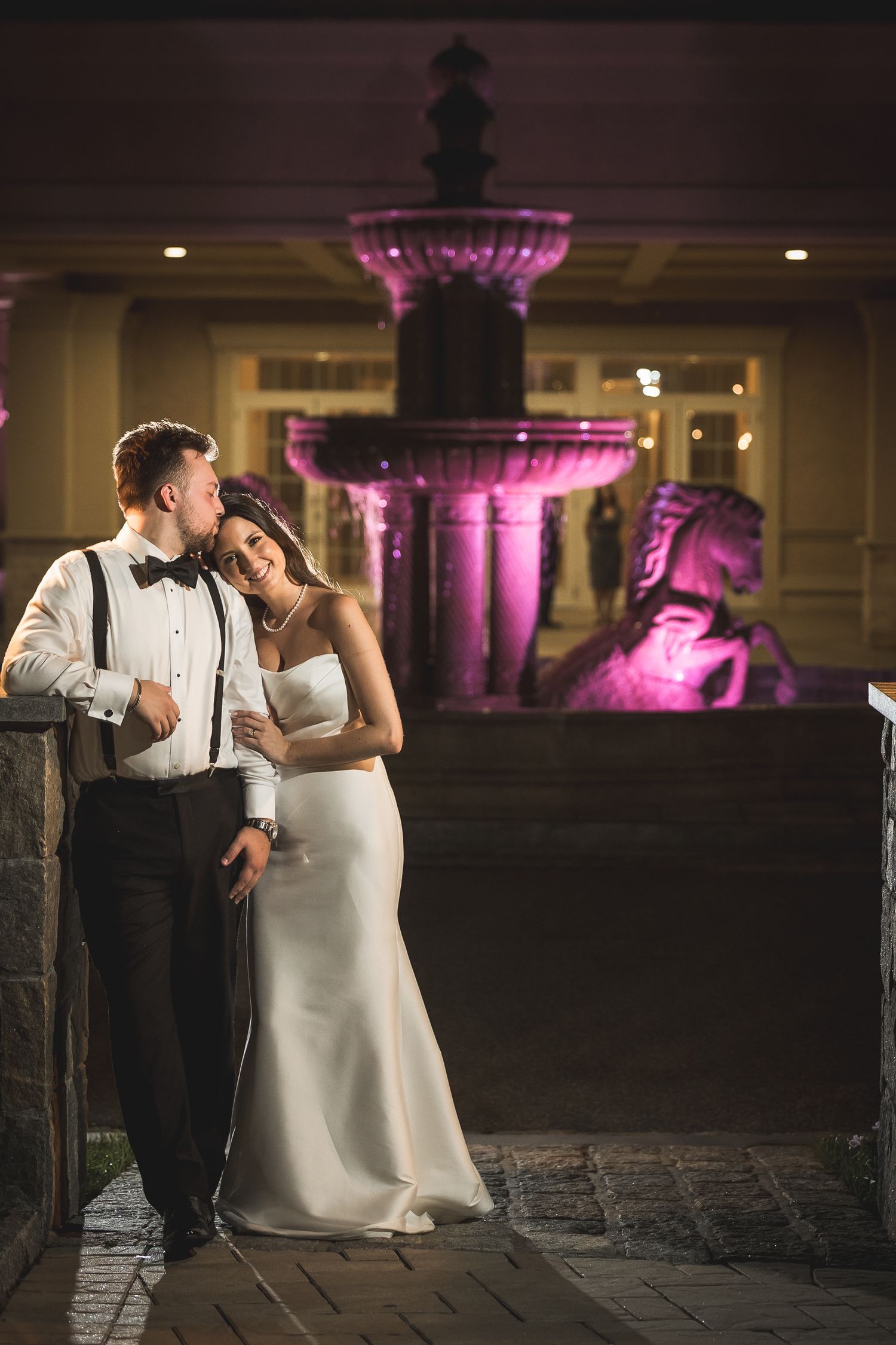 Romantic nighttime portrait with purple uplighting and classical architecture in background.
