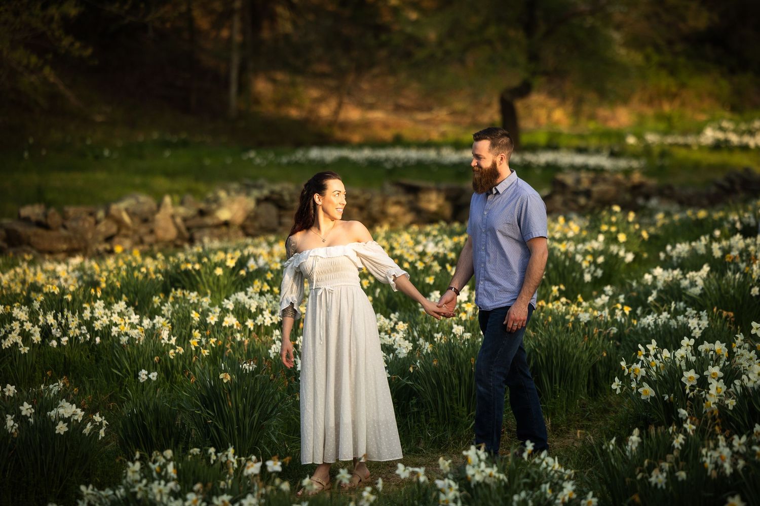 Couple walking through a blooming daffodil field during golden hour in springtime.