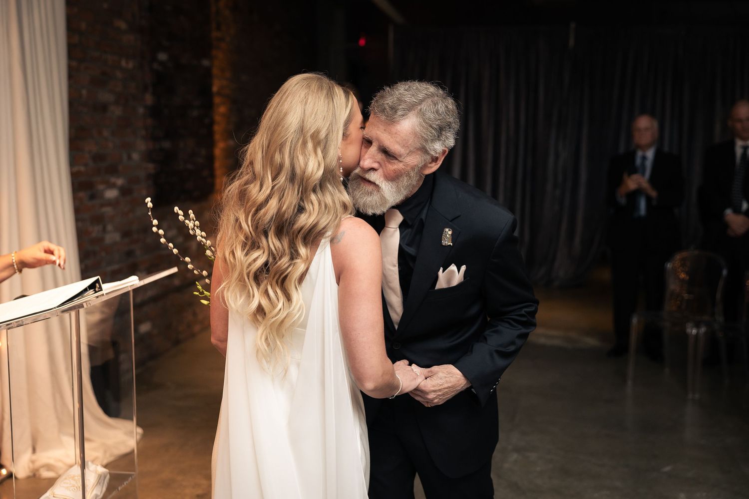 A couple shares a romantic dance together in an elegant dark venue with mood lighting.
