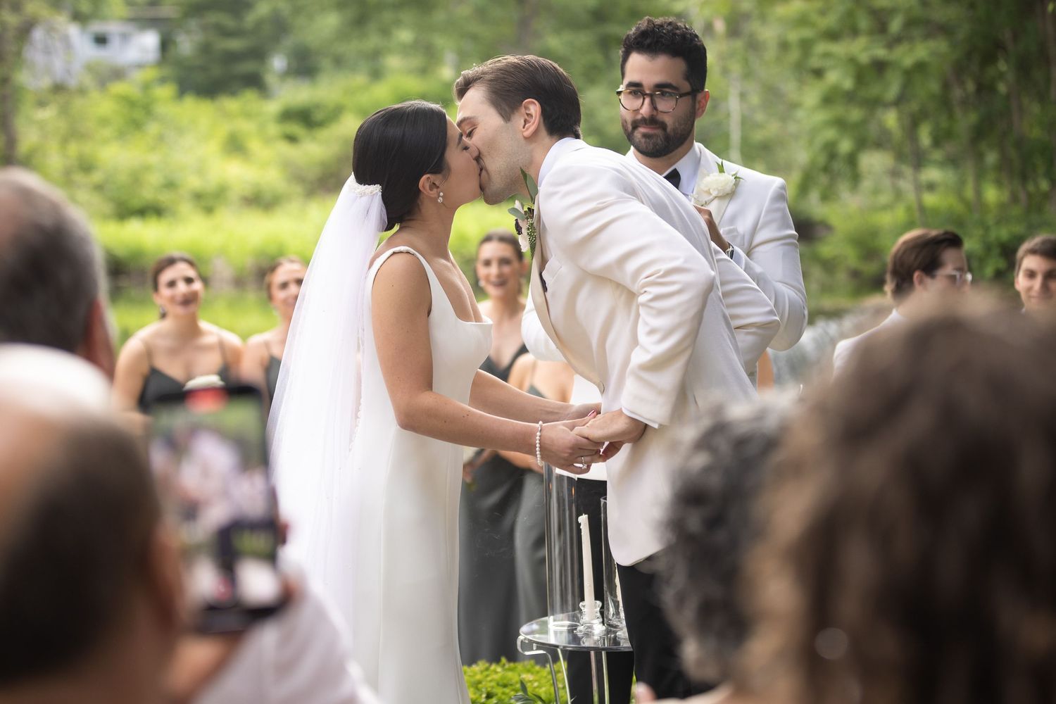 Couple's first kiss at the end of their wedding ceremony photographed through their guests looking on.