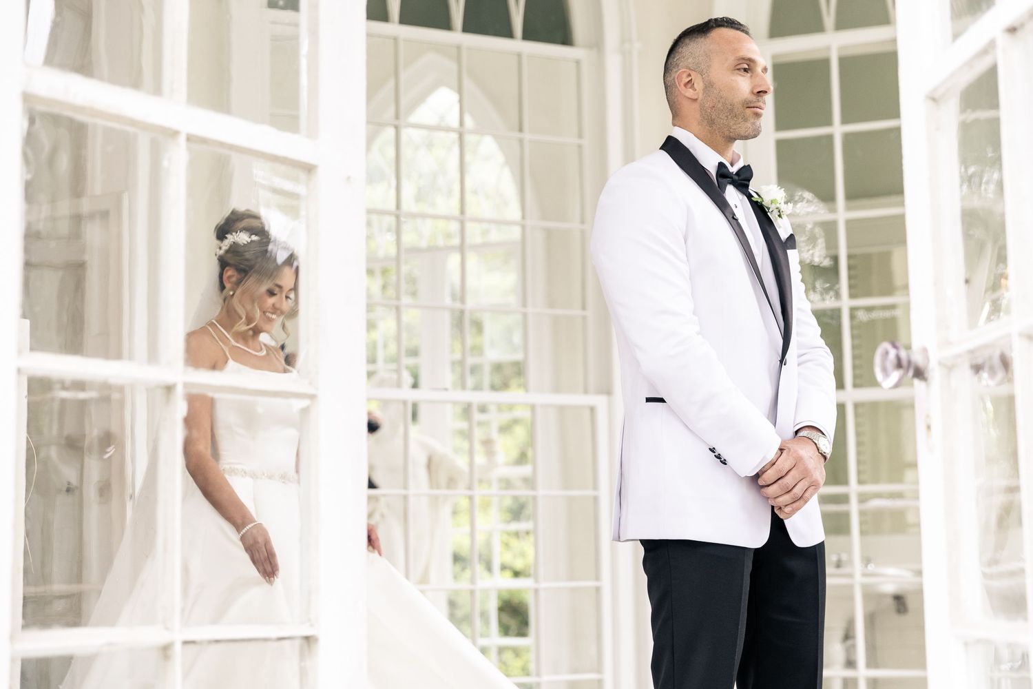 A wedding party poses elegantly in a bright sunlit room with large windows and white decor.